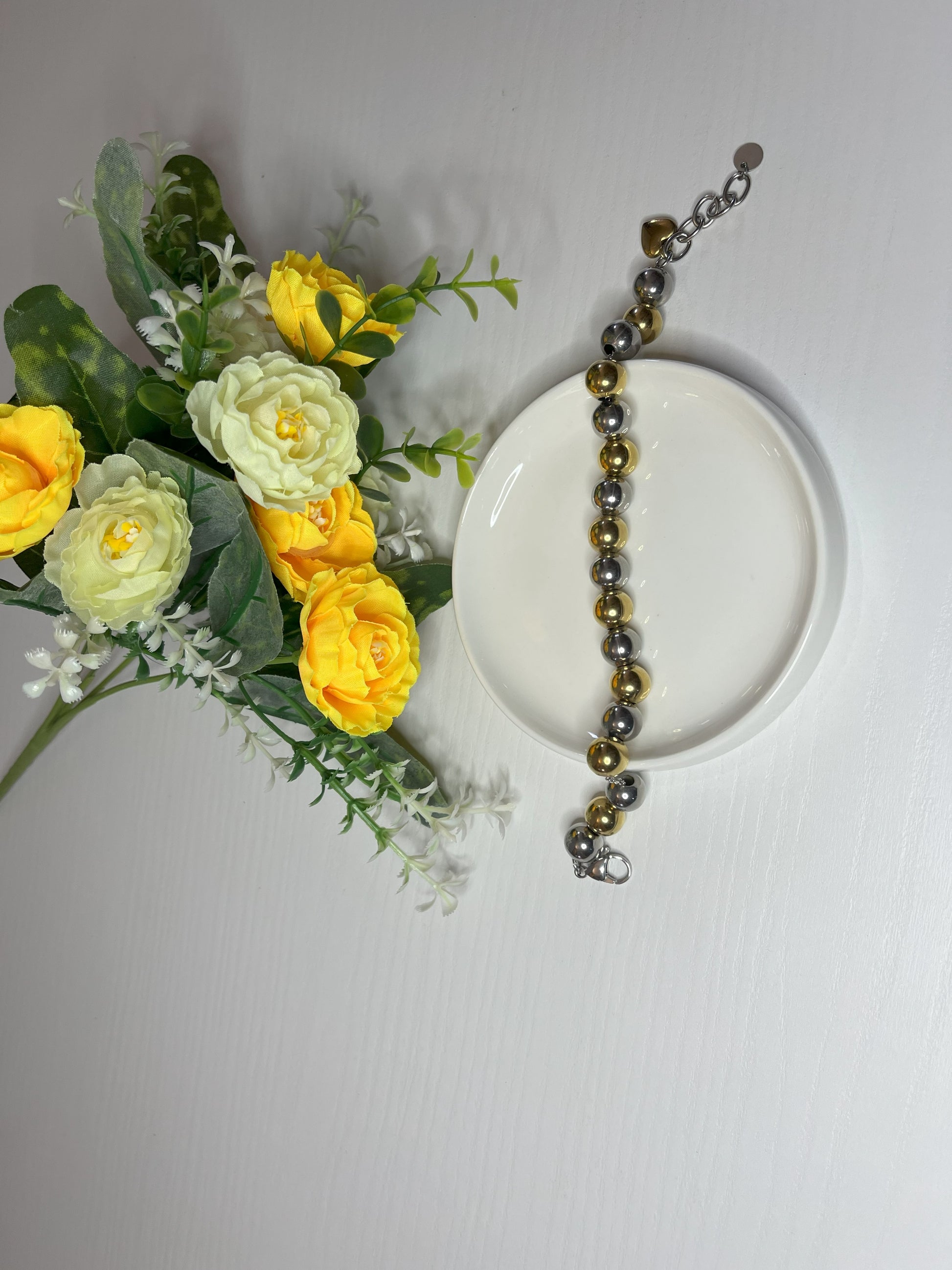 Elegante braccialetto con sfere dorate e argentate lucide su fiori gialli e foglie verdi