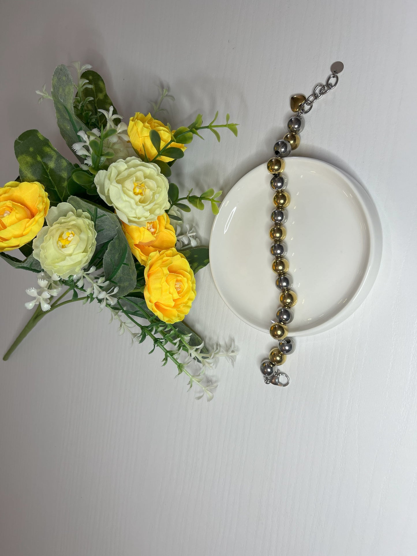Elegante braccialetto con sfere dorate e argentate lucide su fiori gialli e foglie verdi