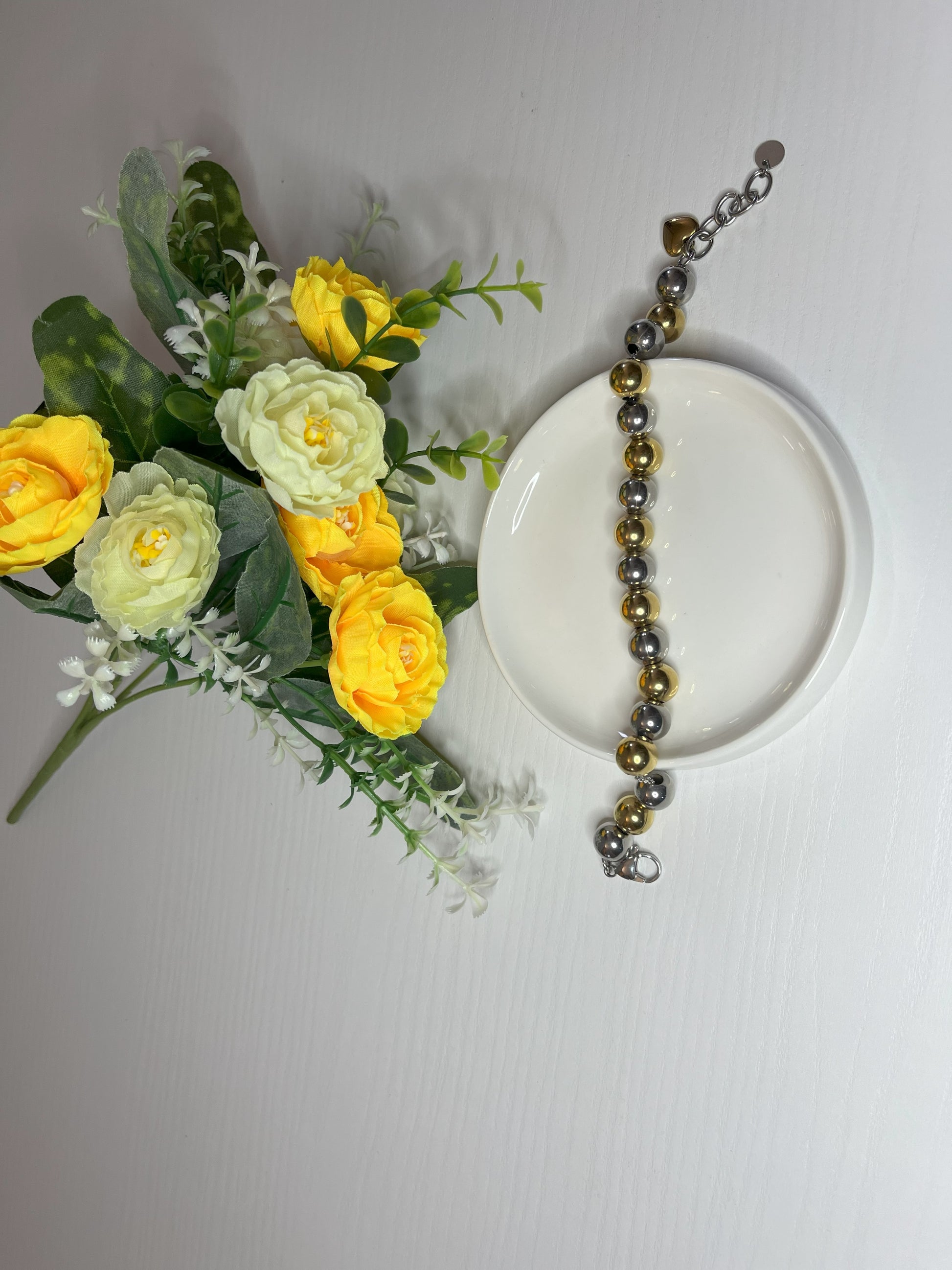 Elegante braccialetto con sfere dorate e argentate lucide su fiori gialli e foglie verdi