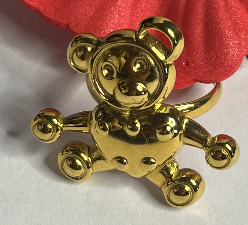 Anello con ciondolo a forma di orsetto, placcato oro, su sfondo bianco con fiore rosso decorativo