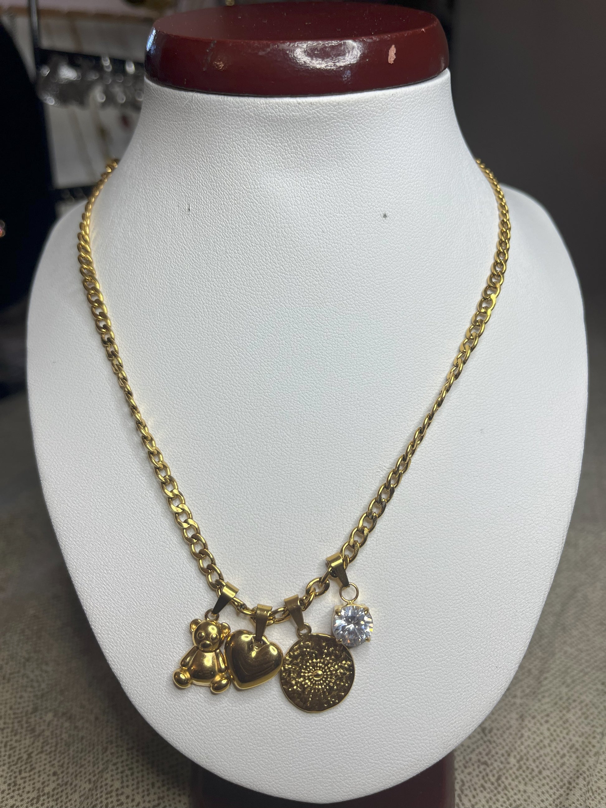 Collana Tesori Dorati in acciaio premium dorato con charm removibili: orsetto, cuore, medaglia decorativa e cristallo brillante su catena elegante. La collana è su espositore bianco