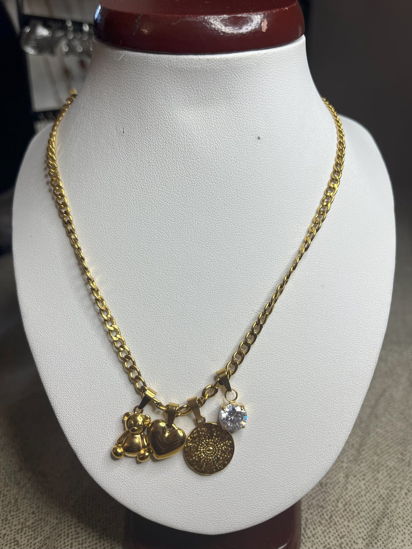 Collana Tesori Dorati in acciaio premium dorato con charm removibili: orsetto, cuore, medaglia decorativa e cristallo brillante su catena elegante. La collana è su espositore bianco