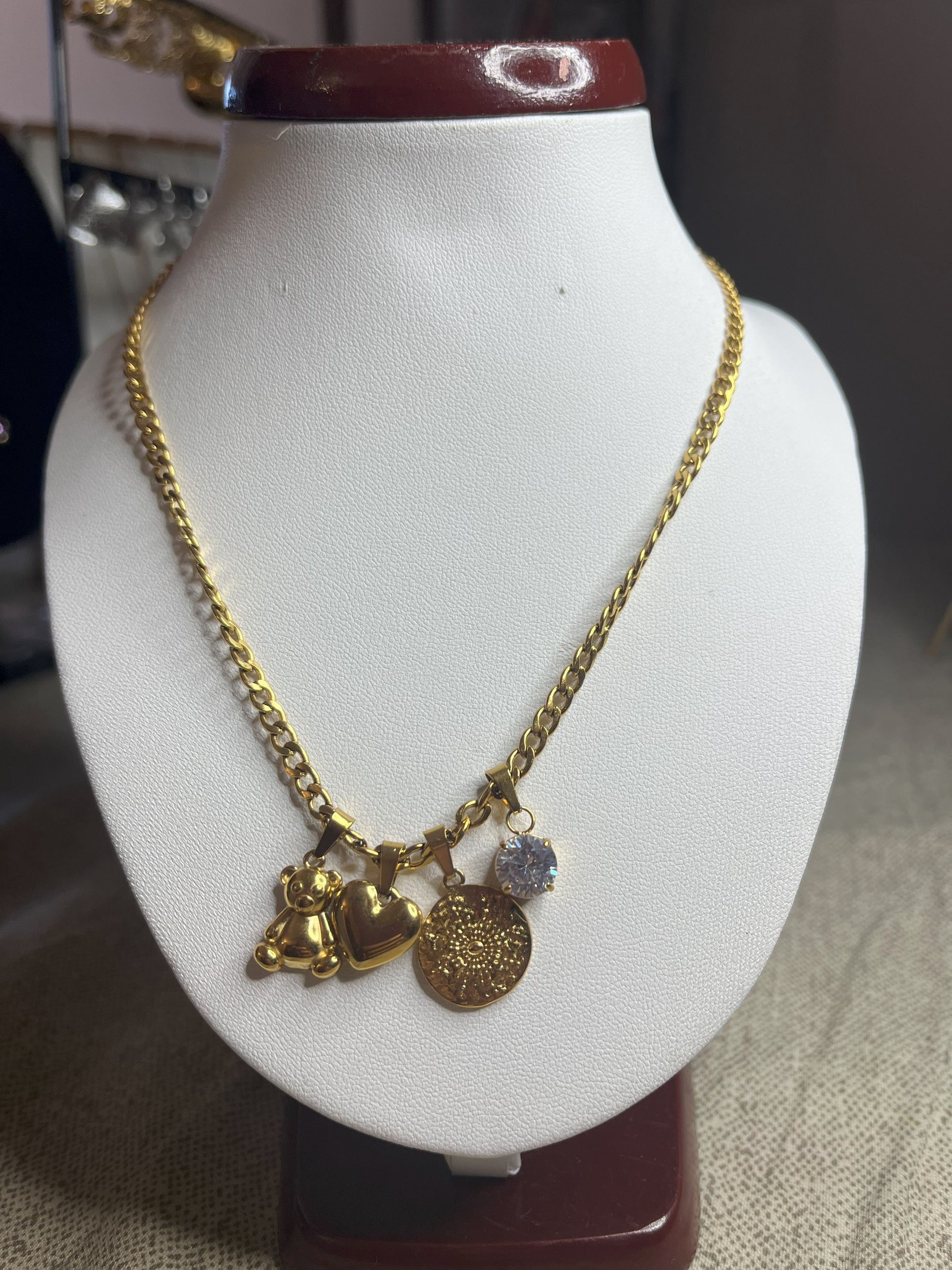 Collana Tesori Dorati in acciaio premium dorato con charm removibili: orsetto, cuore, medaglia decorativa e cristallo brillante su catena elegante. La collana è su espositore bianco