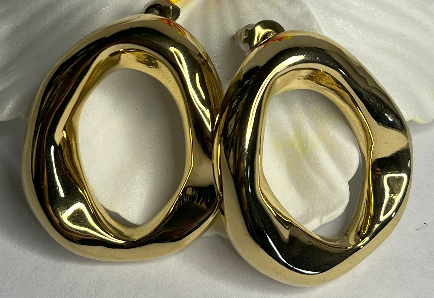 Orecchini Wave premium in due varianti - placcati oro e argento con design organico fluido a forma di onda, fotografati accanto a fiore bianco