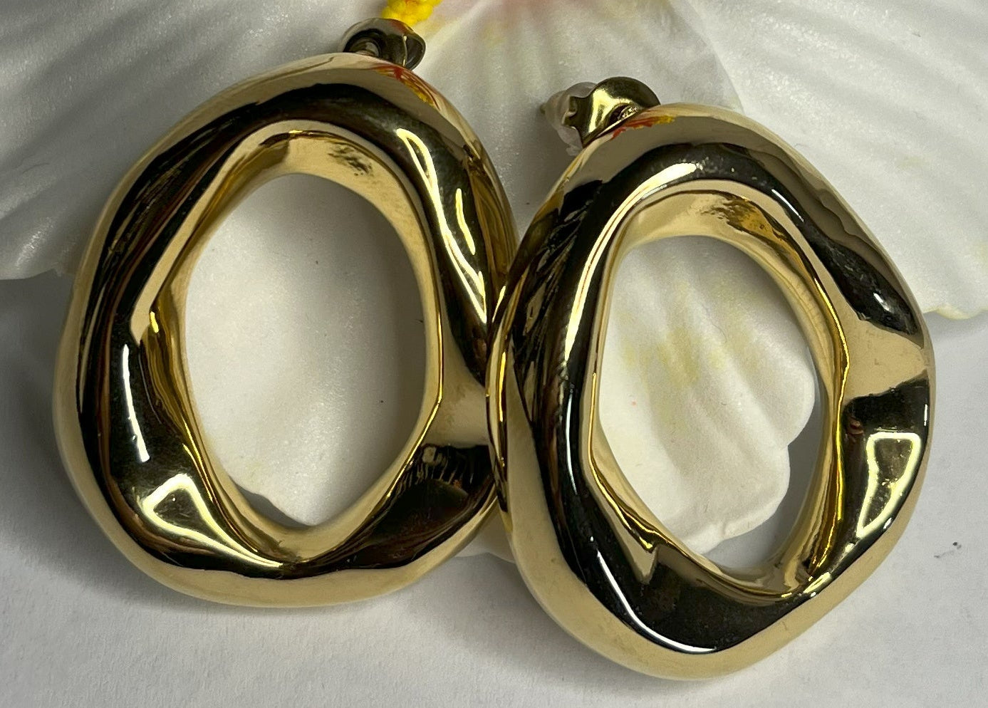 Orecchini Wave premium in due varianti - placcati oro e argento con design organico fluido a forma di onda, fotografati accanto a fiore bianco