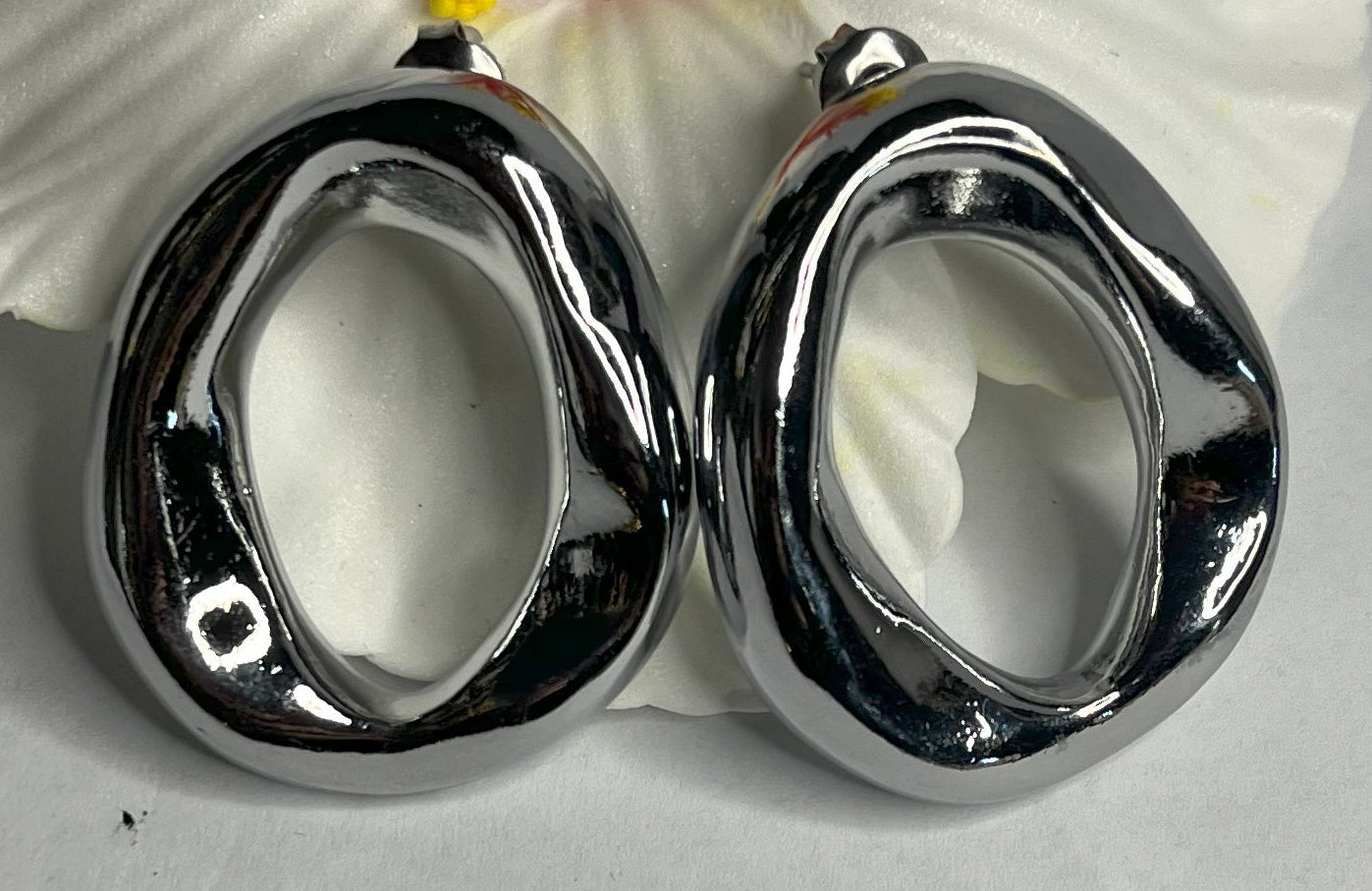 Orecchini Wave premium in due varianti - placcati oro e argento con design organico fluido a forma di onda, fotografati accanto a fiore bianco