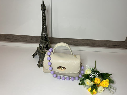 Mini-Parisienne borsa beige compatta con collana di perle viola coordinata, accanto a Torre Eiffel decorativa e fiori gialli