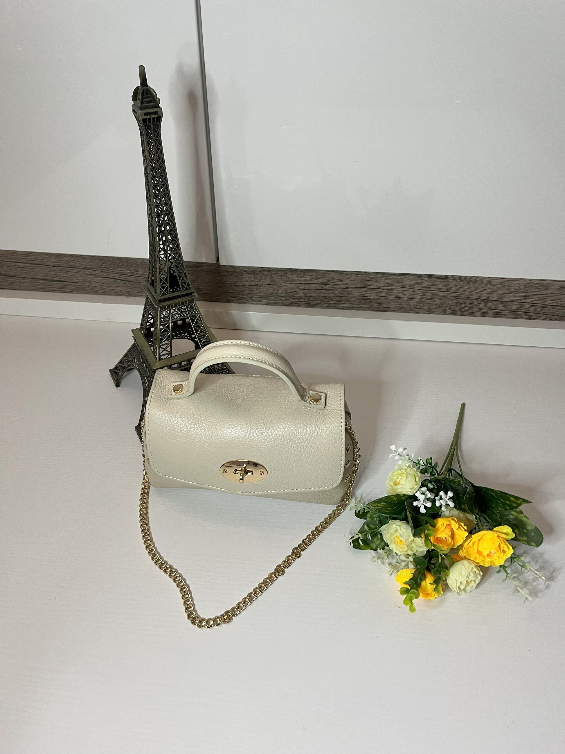 Mini-Parisienne borsa beige compatta con collana di perle viola coordinata, accanto a Torre Eiffel decorativa e fiori gialli
