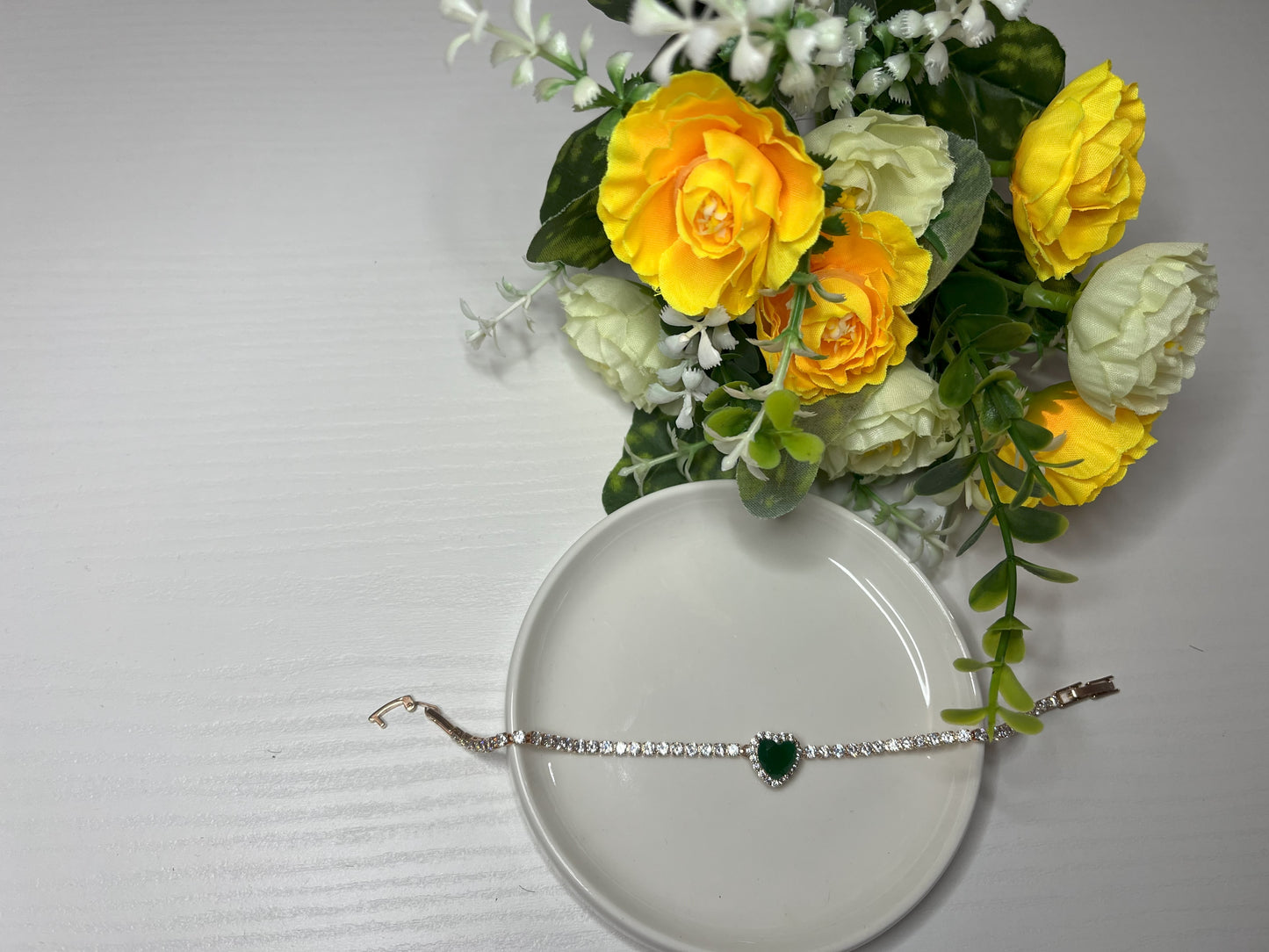 Elegante braccialetto tennis con cristalli brillanti e pietra verde smeraldo centrale, indossato al polso su sfondo tessuto bianco