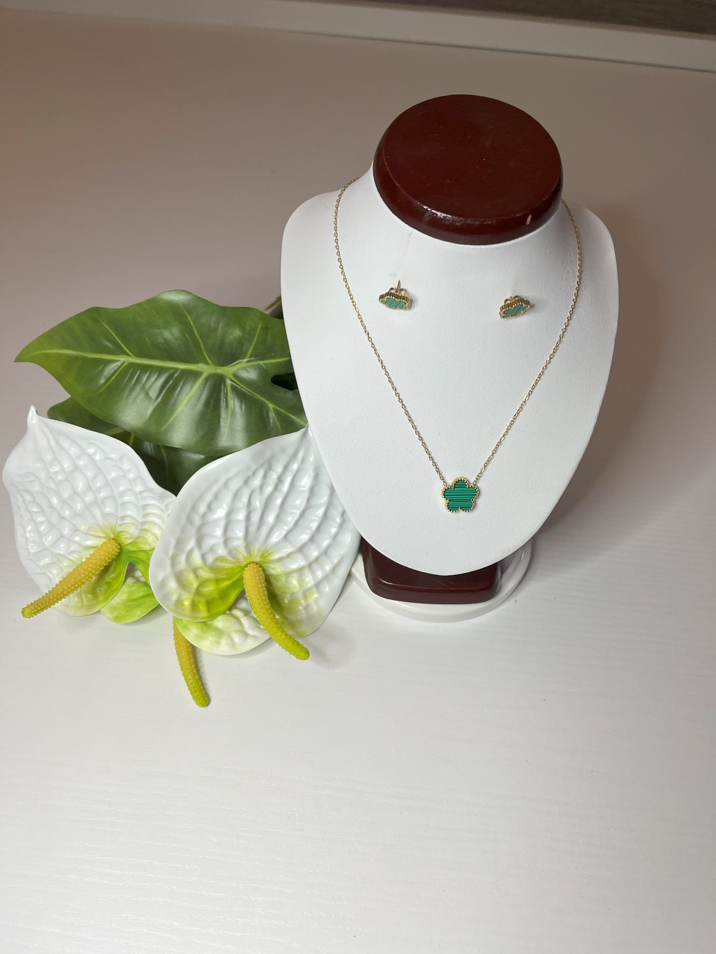 Set Elegance con collana e orecchini coordinati con pietre verdi smeraldo su catena dorata, esposto su busto bianco con decorazioni floreali
