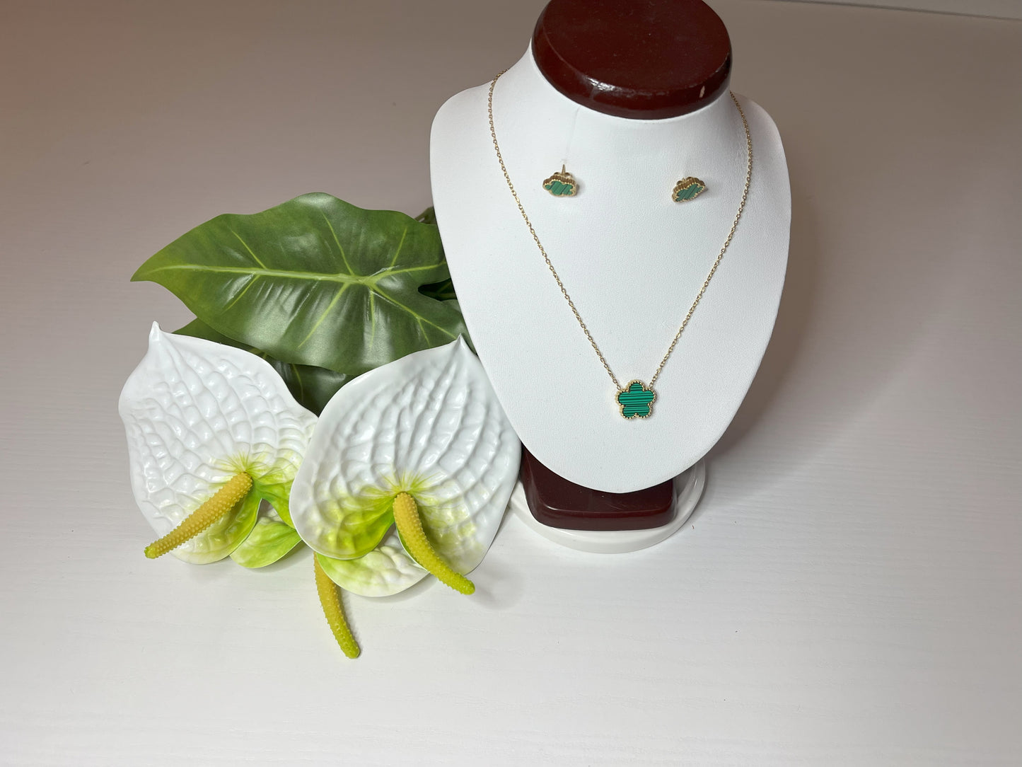 Set Elegance con collana e orecchini coordinati con pietre verdi smeraldo su catena dorata, esposto su busto bianco con decorazioni floreali