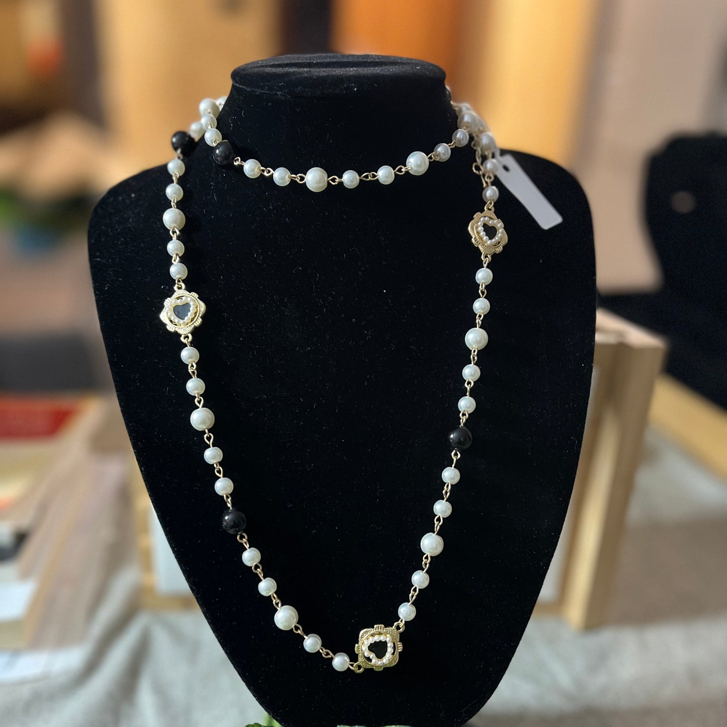 Collana di perle bianche con tre ciondoli a forma di cuore sacro dorati esposta su busto nero