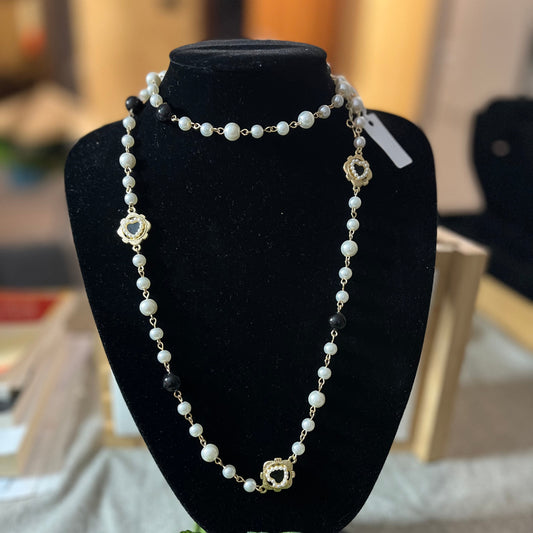 Collana di perle bianche con tre ciondoli a forma di cuore sacro dorati esposta su busto nero