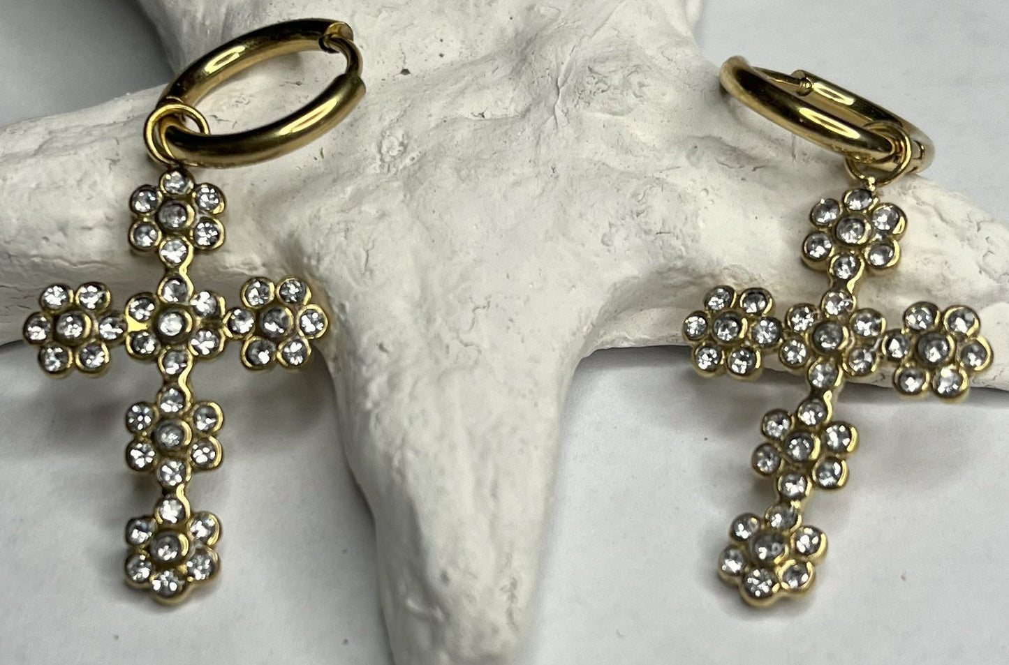 Orecchini pendenti con ciondoli a croce decorati con cristalli diamantati e ganci dorati, appoggiati su stella marina bianca