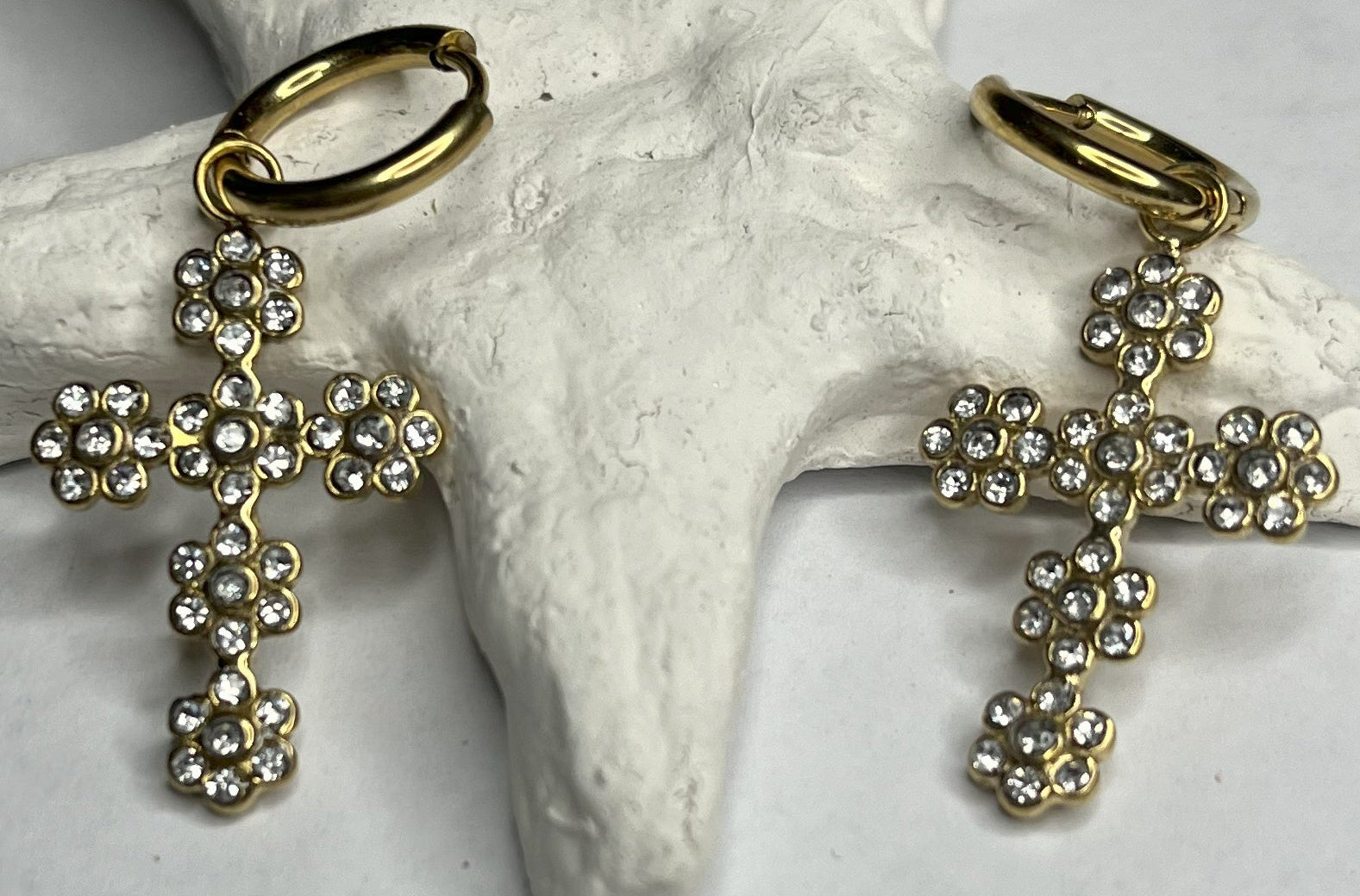 Orecchini pendenti con ciondoli a croce decorati con cristalli diamantati e ganci dorati, appoggiati su stella marina bianca
