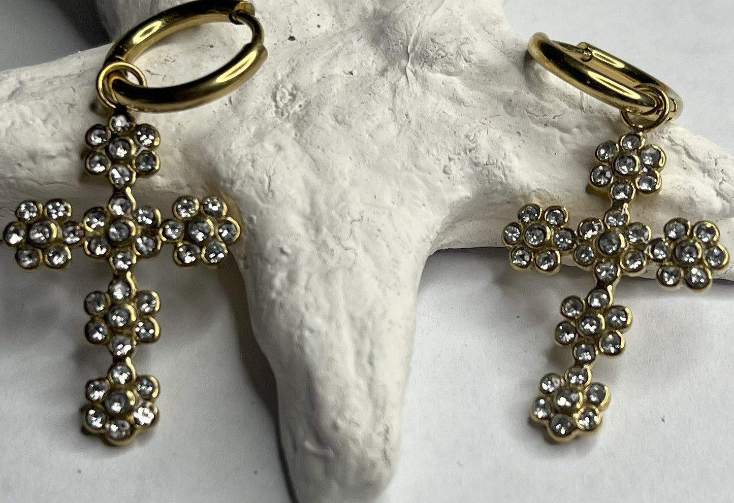 Orecchini pendenti con ciondoli a croce decorati con cristalli diamantati e ganci dorati, appoggiati su stella marina bianca