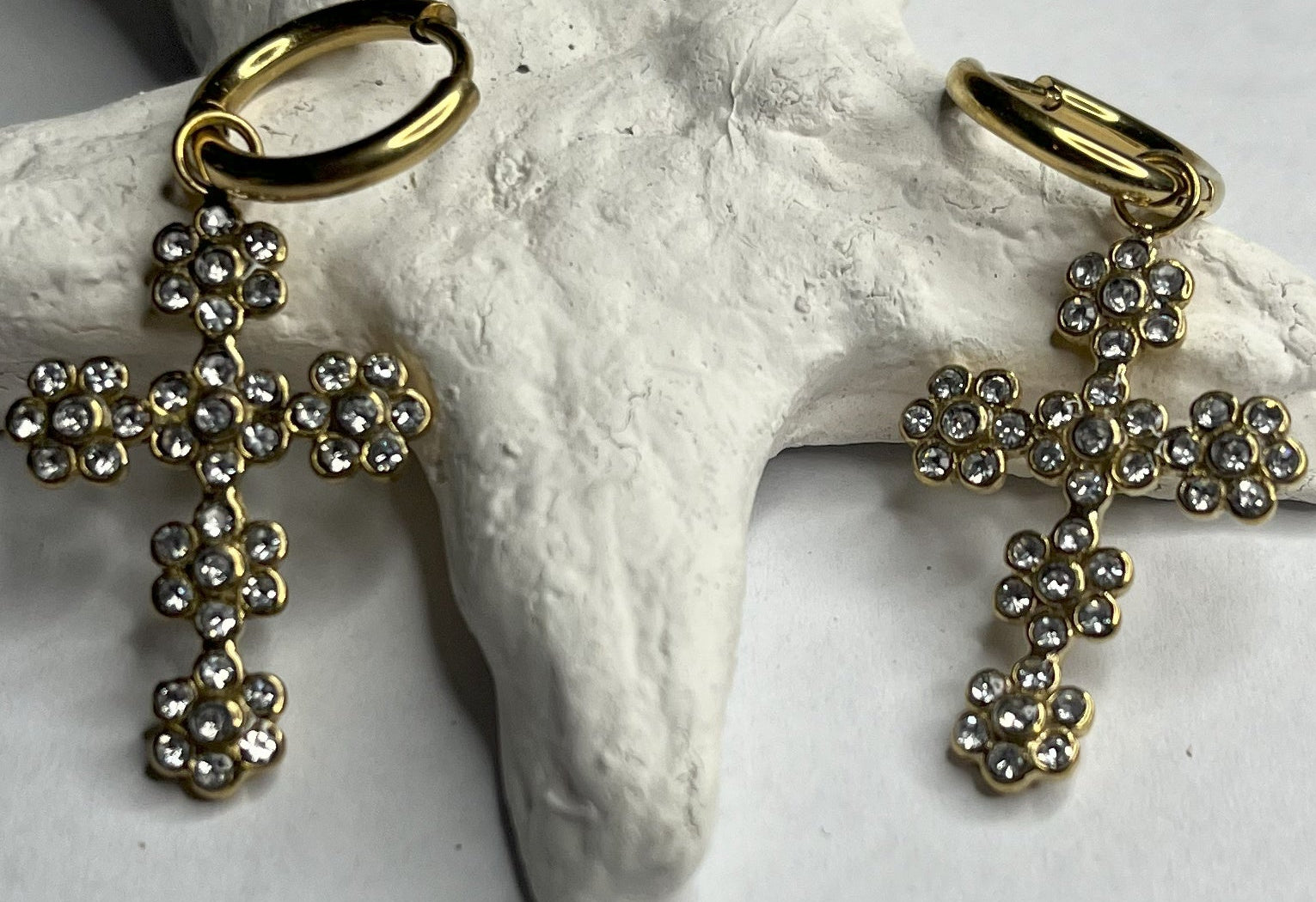 Orecchini pendenti con ciondoli a croce decorati con cristalli diamantati e ganci dorati, appoggiati su stella marina bianca