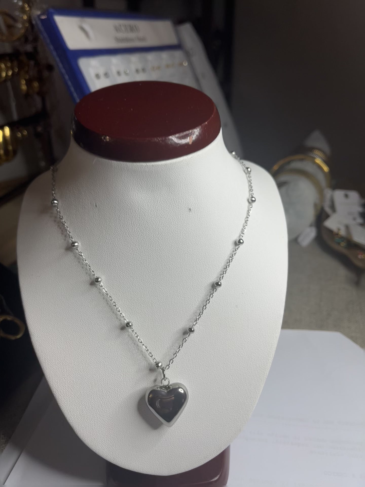 Collana Allegra in acciaio premium con catena decorata da sfere e ciondolo cuore, variante placcato argento, esposta su busto espositore bianco