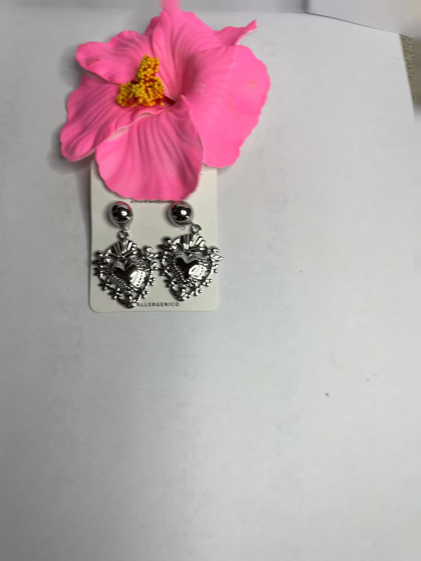 Orecchini dorati a forma di sacro cuore con dettagli intarsiati e lavorazione artigianale su sfondo con fiore rosa