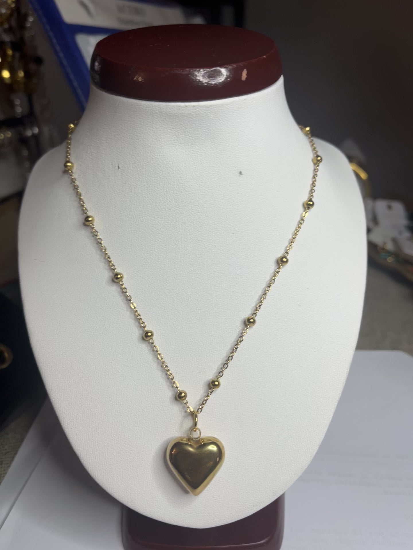 Collana Allegra in acciaio premium con catena decorata da sfere e ciondolo cuore, variante placcato oro, esposta su busto espositore bianco
