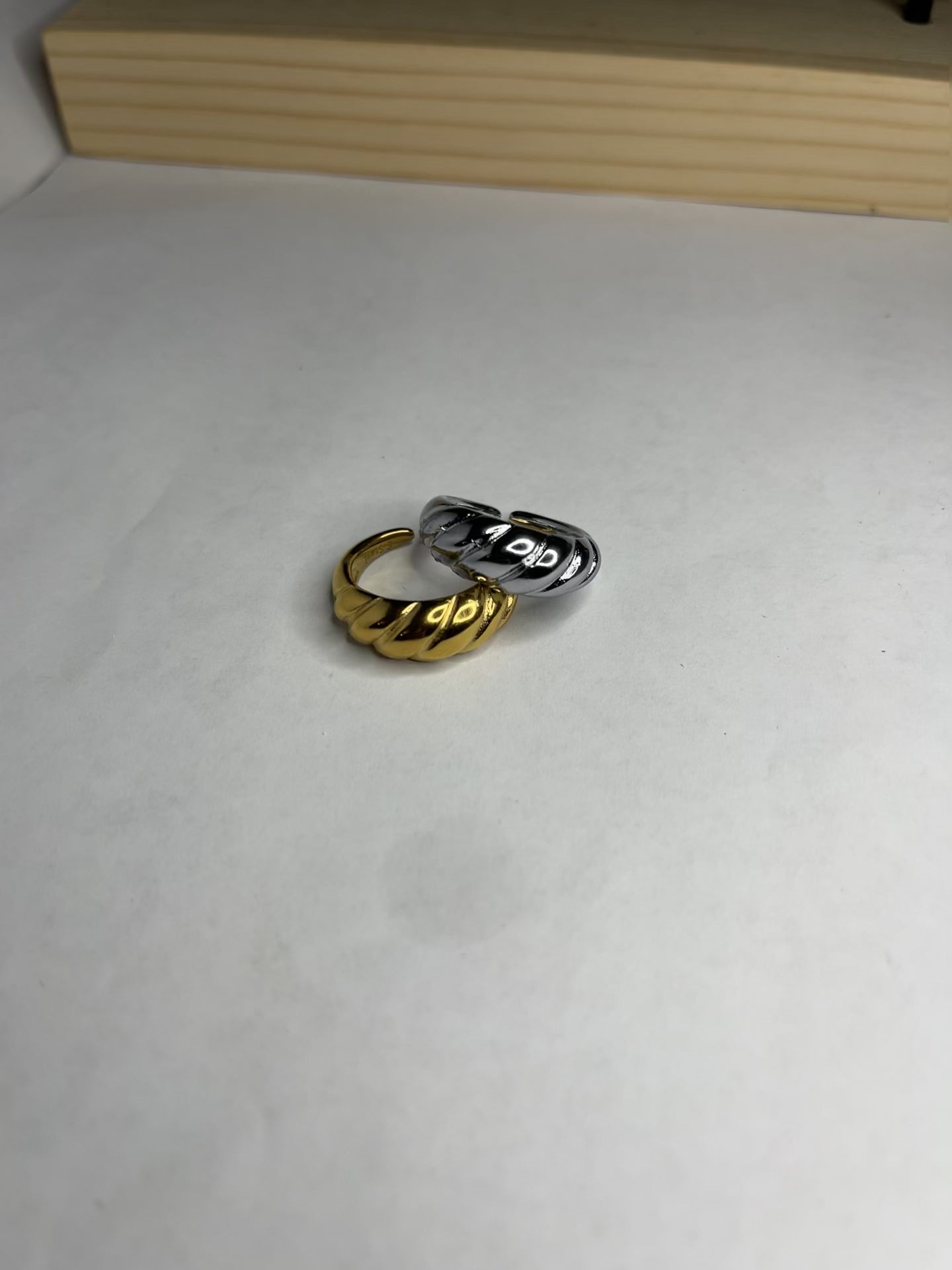 Anello con design intrecciato placcato oro, texture tridimensionale su sfondo neutro