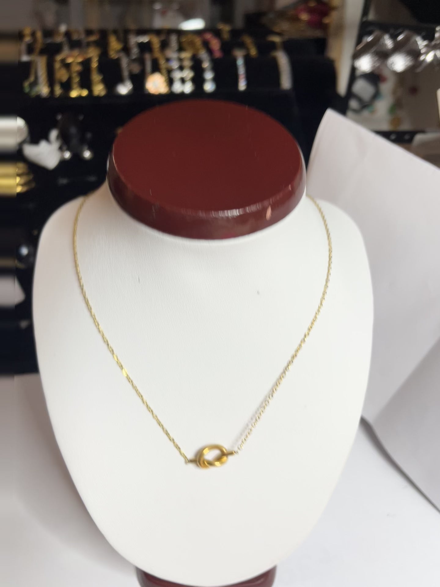 Collana Love Knot con pendente a nodo intrecciato dorato su catena delicata, simbolo di amore eterno esposto su busto bianco