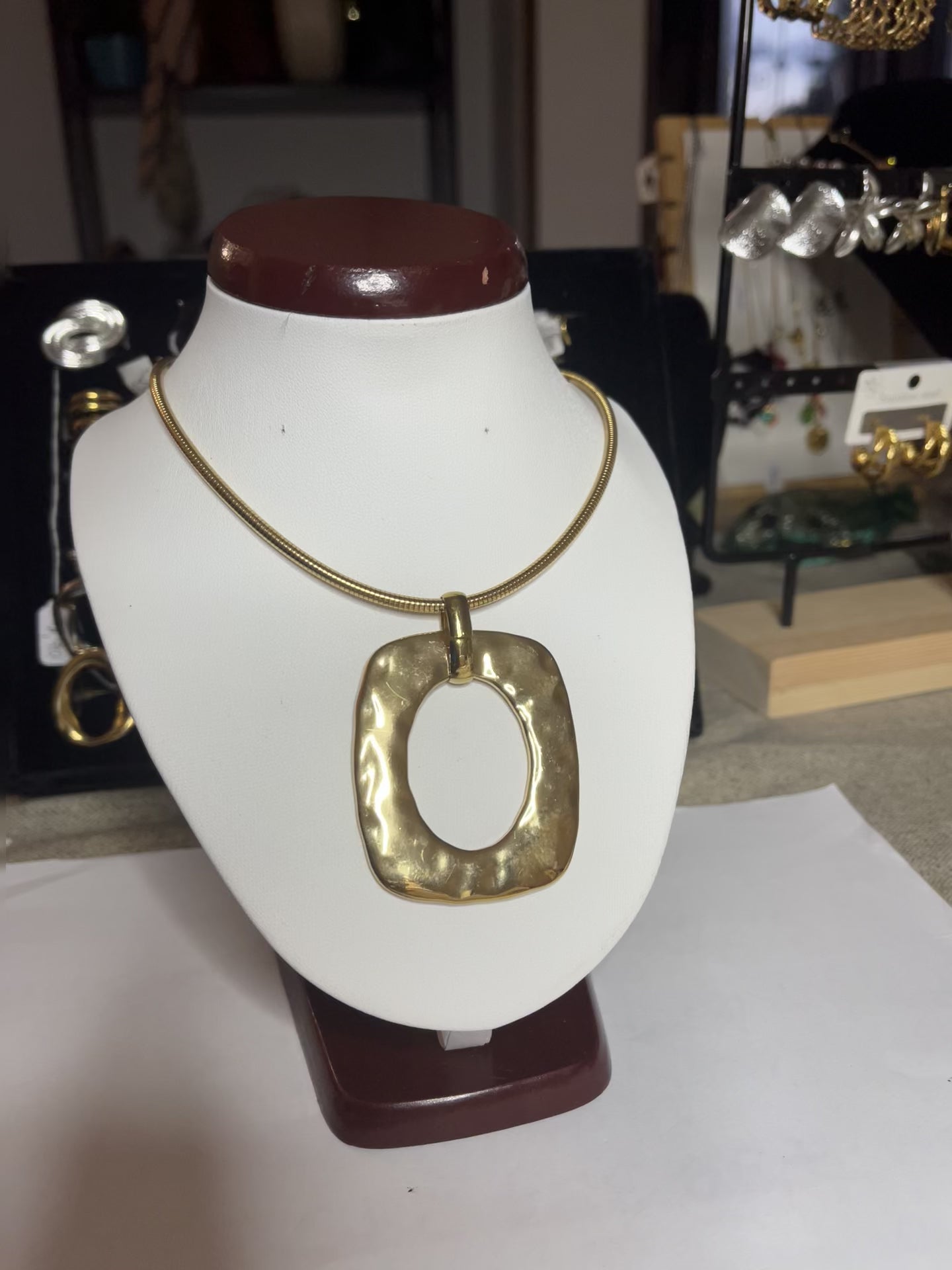 Collana Charlize in acciaio inossidabile placcato oro con catena a maglia serpente e pendente geometrico quadrato, esposta su busto bianco