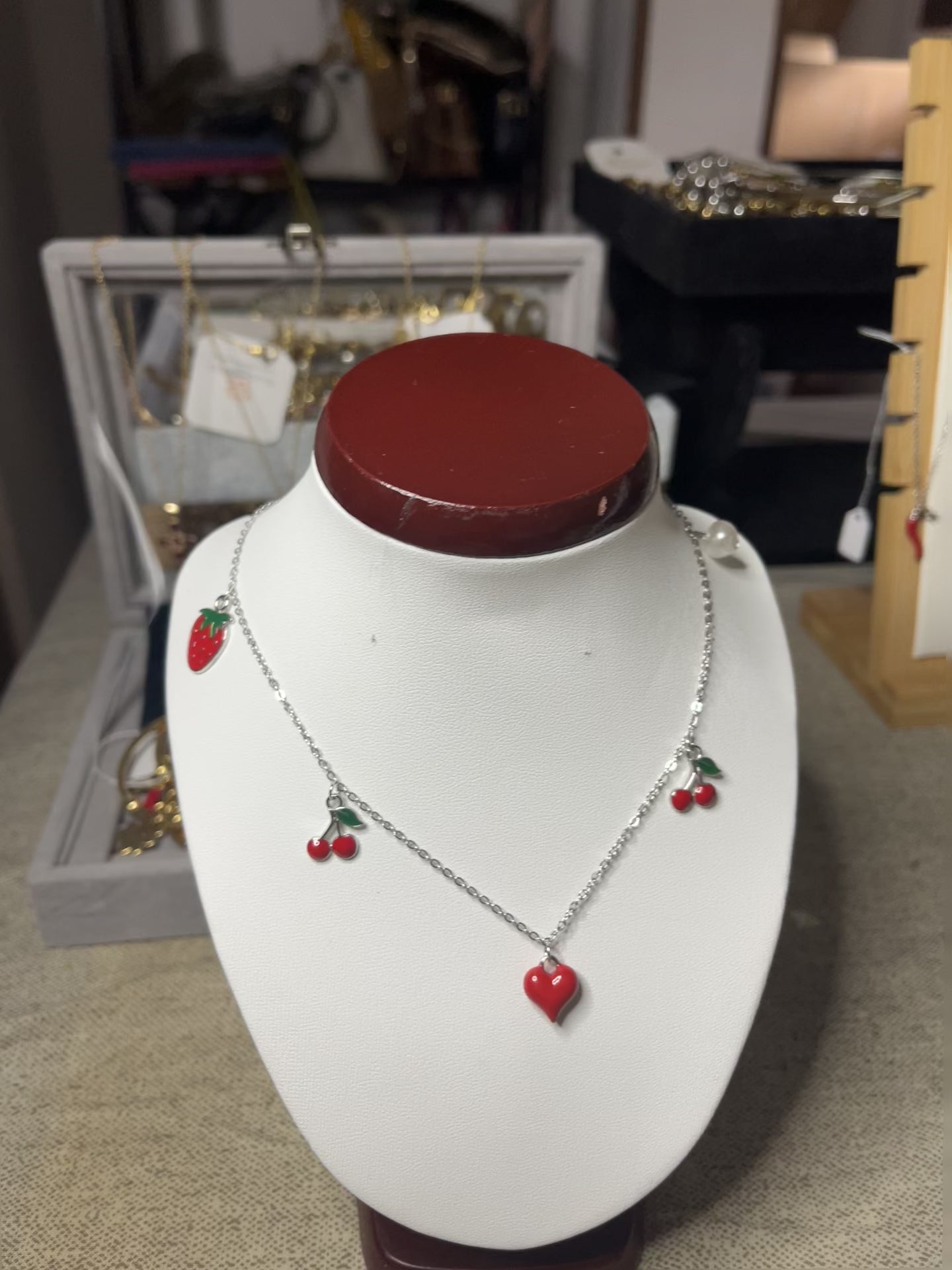 Collana Good Vibes con catena argentata e ciondoli colorati a forma di cuore, ciliegie e fragola, esposta su busto porta gioielli bianco