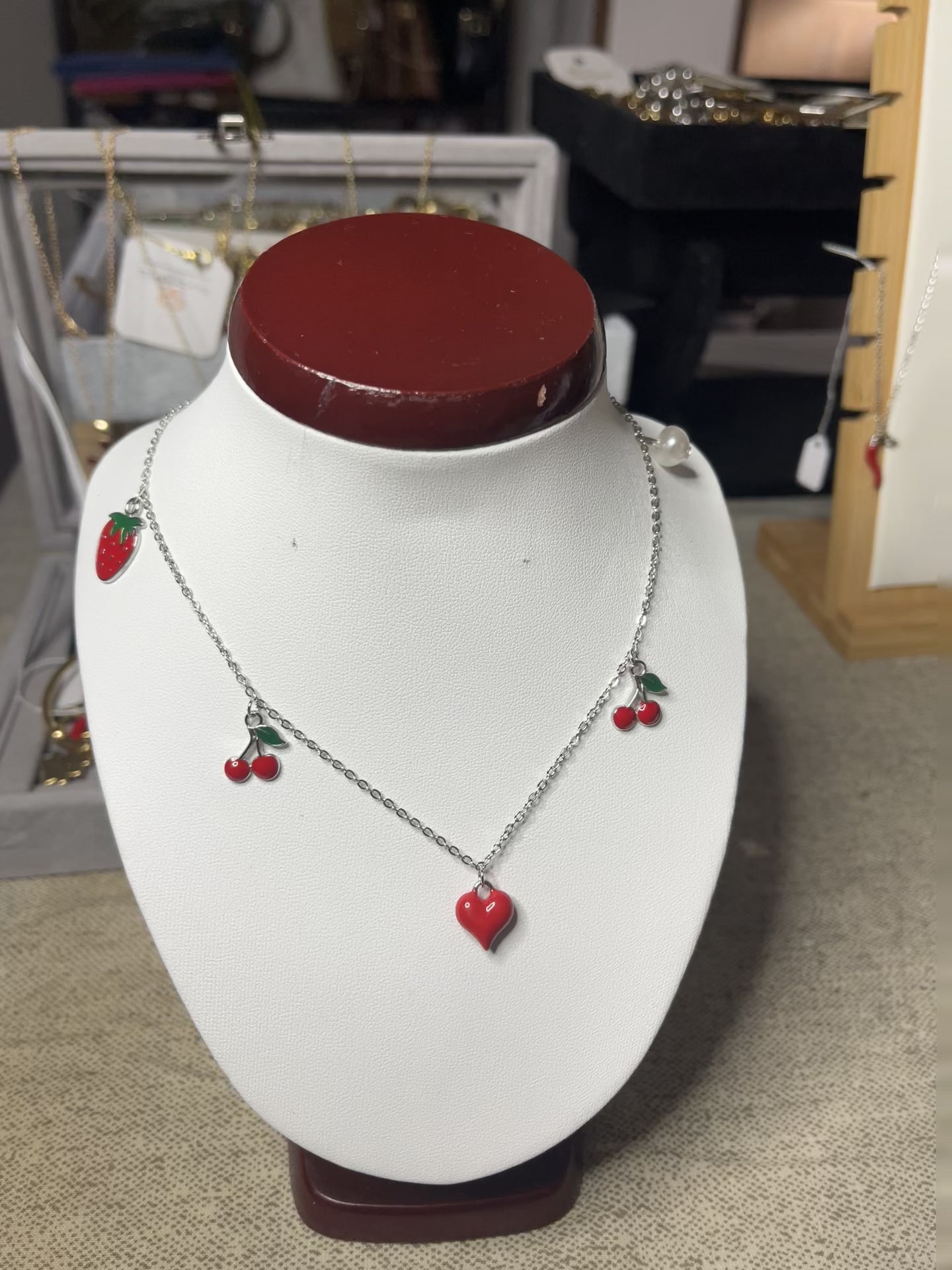 Collana Good Vibes con catena argentata e ciondoli colorati a forma di cuore, ciliegie e fragola, esposta su busto porta gioielli bianco