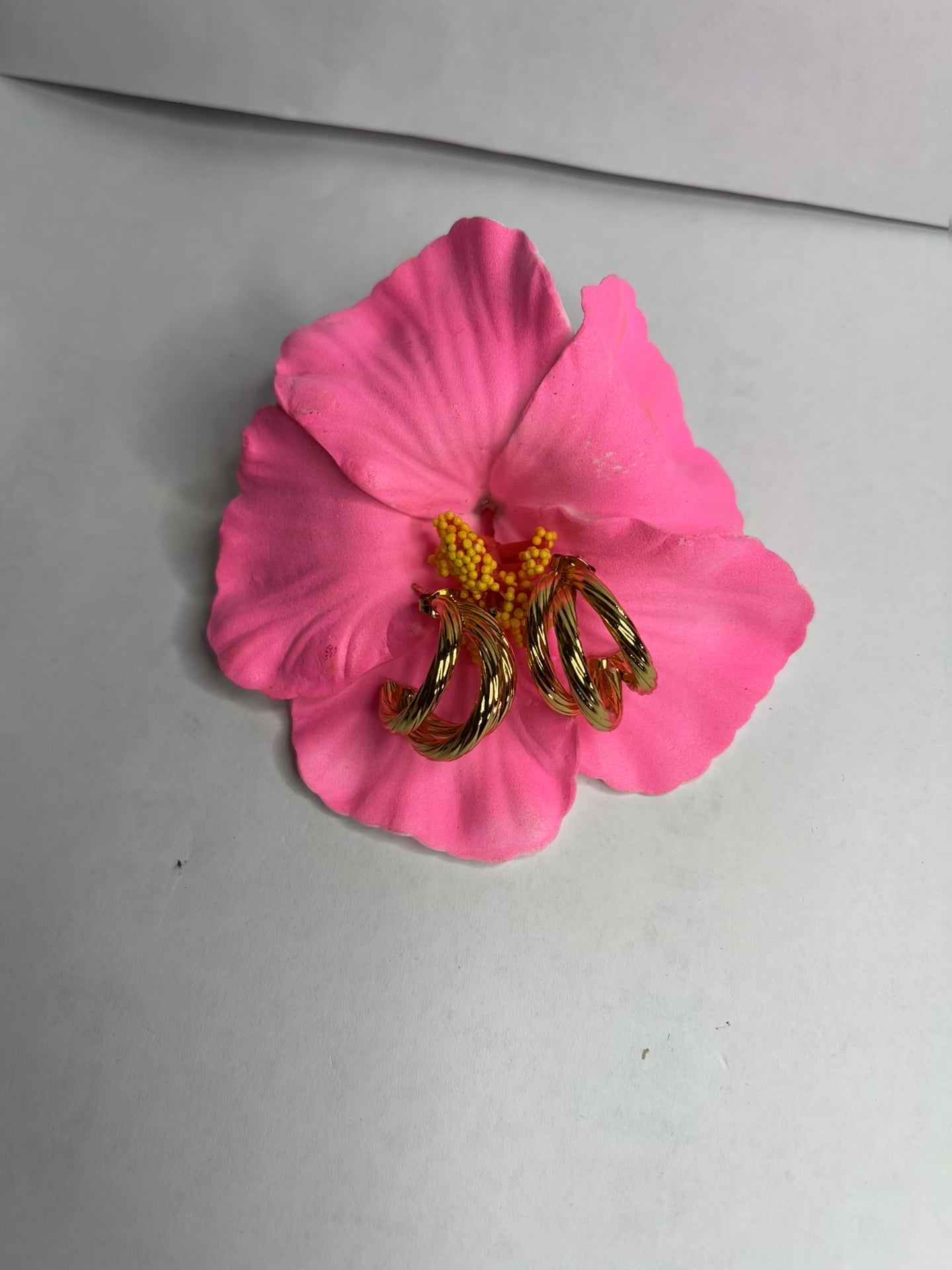 Orecchini Helix placcati oro premium con design a spirale tridimensionale, fotografati su petali di fiore rosa fucsia