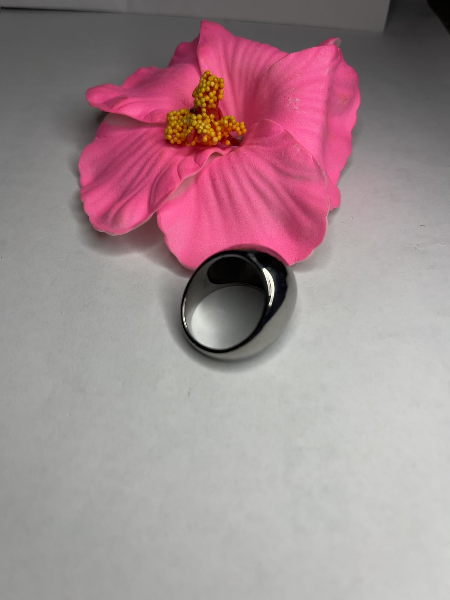Anello Riflesso Argento in acciaio inossidabile con finitura a specchio lucida, design ovale elegante, fotografato su petalo di fiore rosa che ne esalta la brillantezza