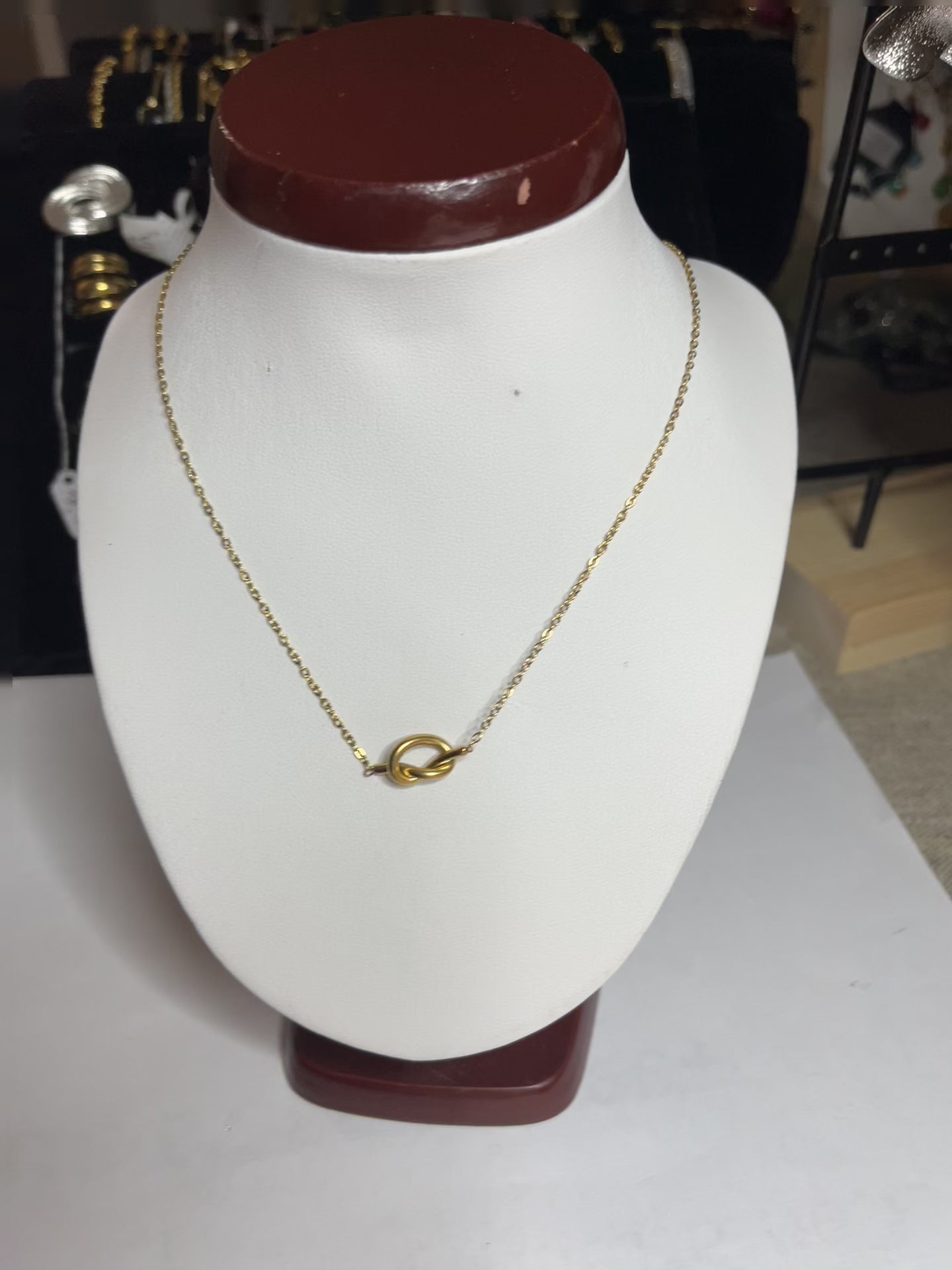 Collana Love Knot con pendente a nodo intrecciato dorato su catena delicata, simbolo di amore eterno esposto su busto bianco