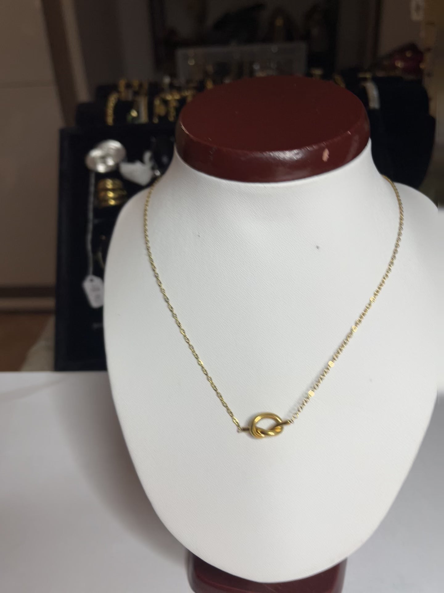 Collana Love Knot con pendente a nodo intrecciato dorato su catena delicata, simbolo di amore eterno esposto su busto bianco