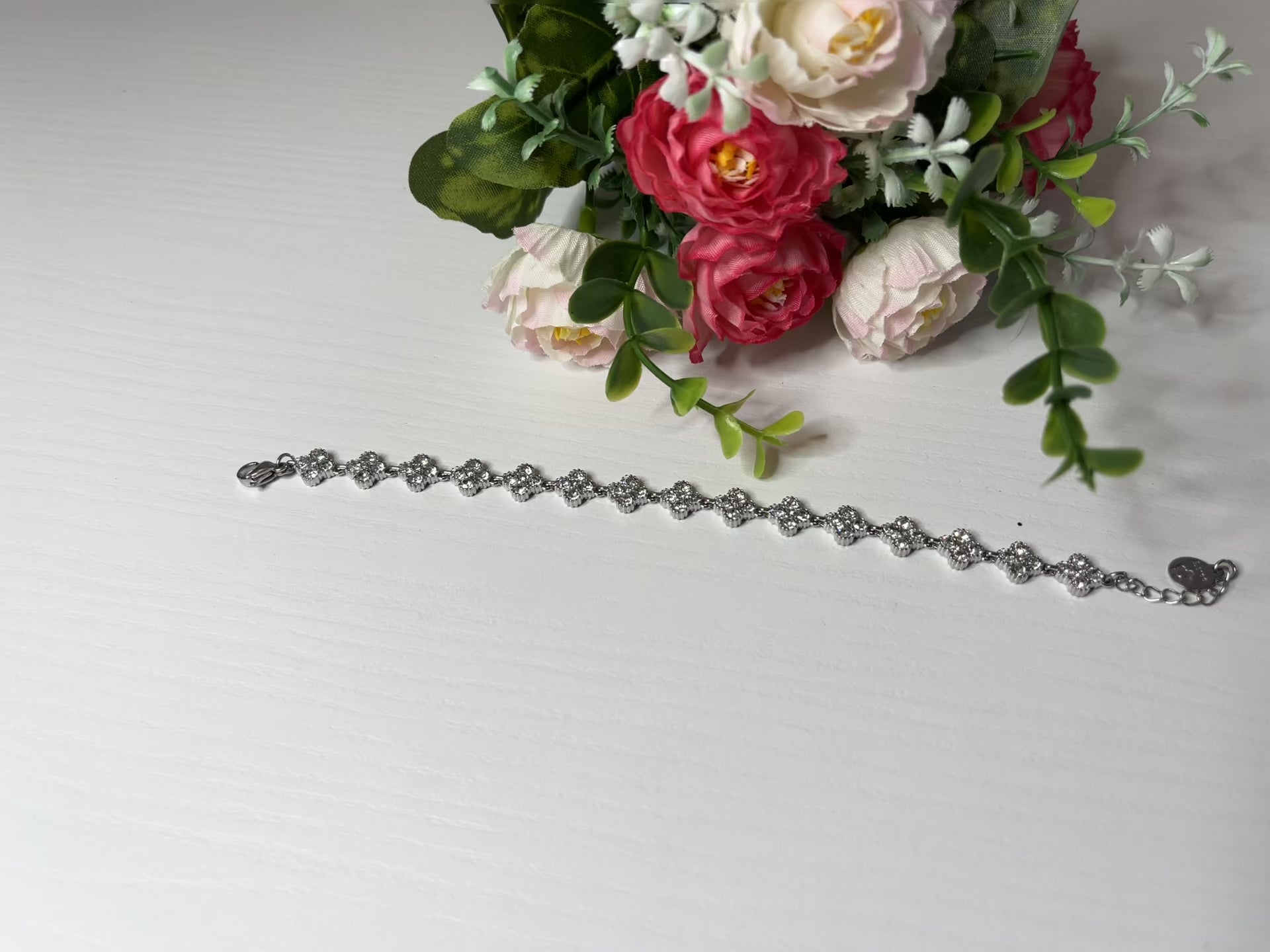 Braccialetto tennis placcato argento con quadrifogli portafortuna e cristalli scintillanti su sfondo bianco con foglie verdi