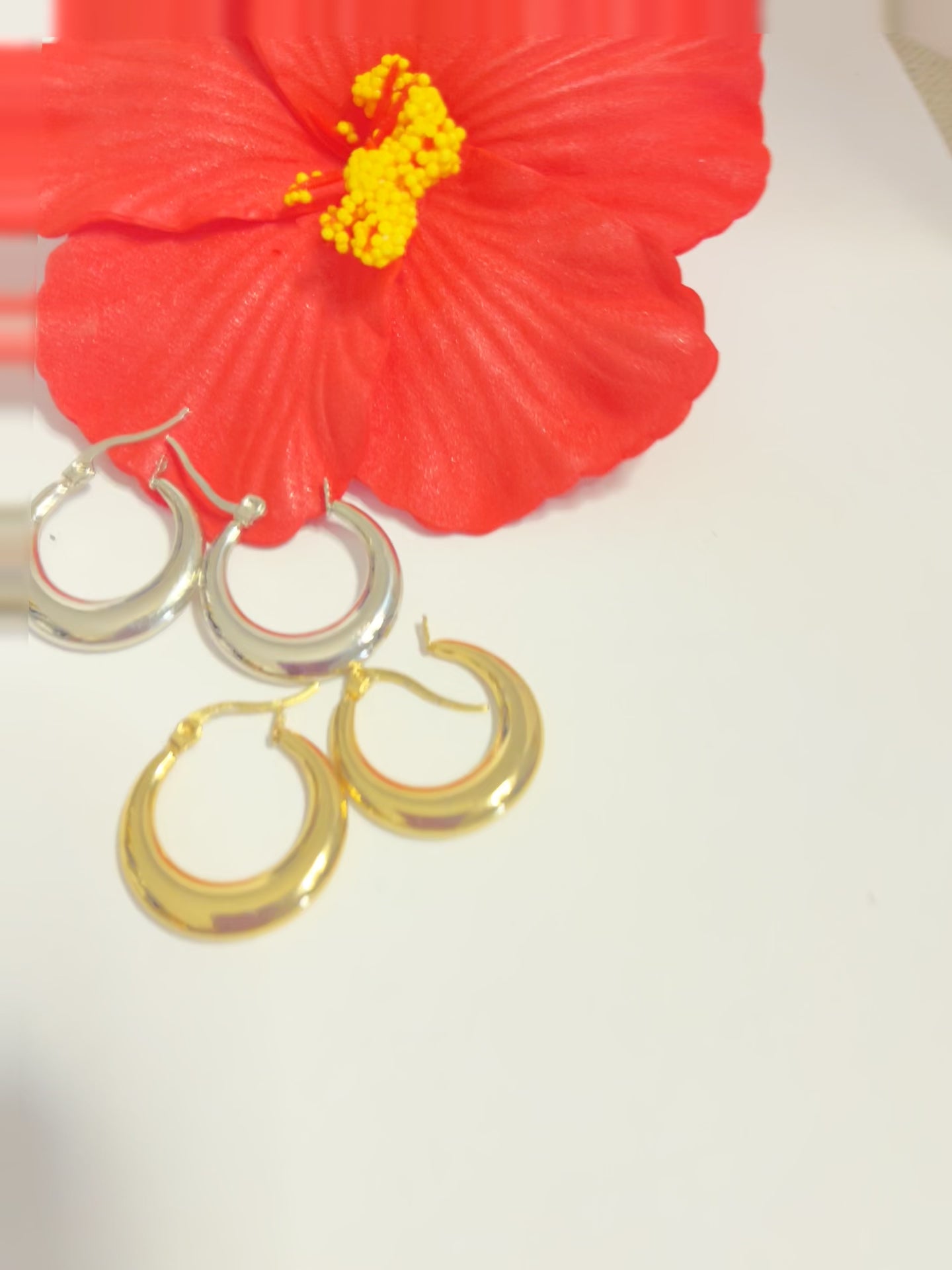 Set di orecchini creoli placcati, due paia in oro e argento, disposti su sfondo neutro con fiore rosso decorativo