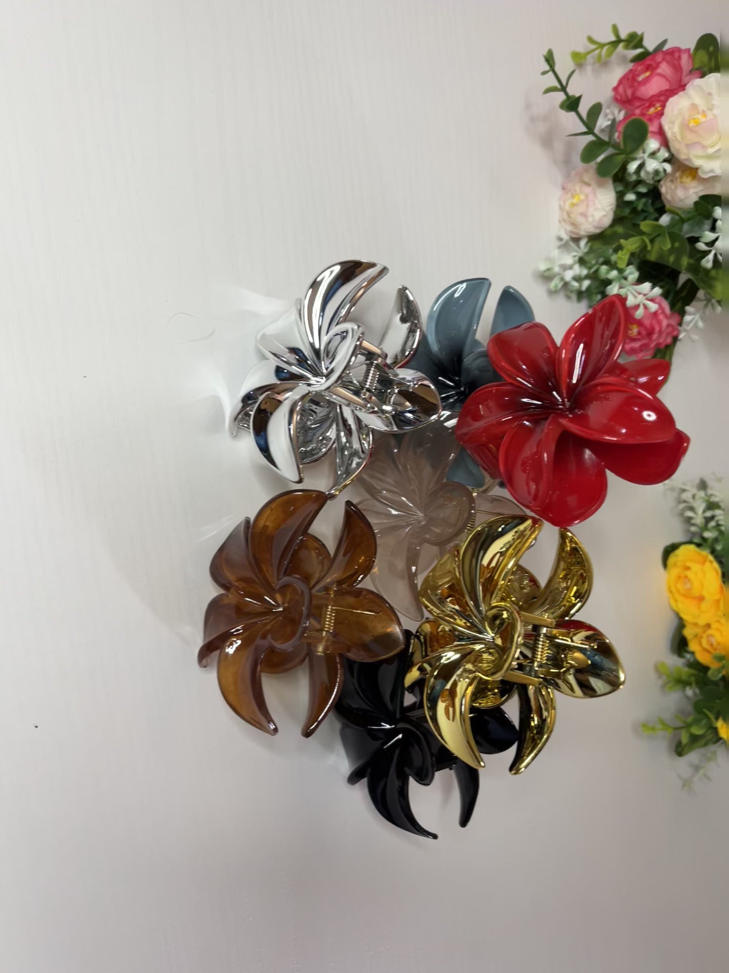 Elegante pinza hawaiana per capelli a forma di fiore con petali lucidi, posizionata accanto a un bouquet di fiori freschi gialli e bianchi