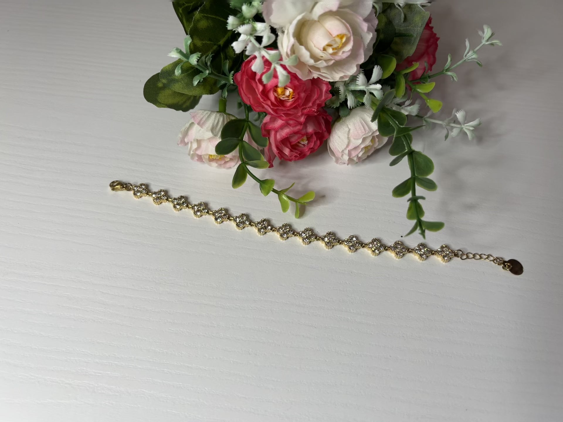Braccialetto tennis placcato argento con quadrifogli portafortuna e cristalli scintillanti su sfondo bianco con foglie verdi