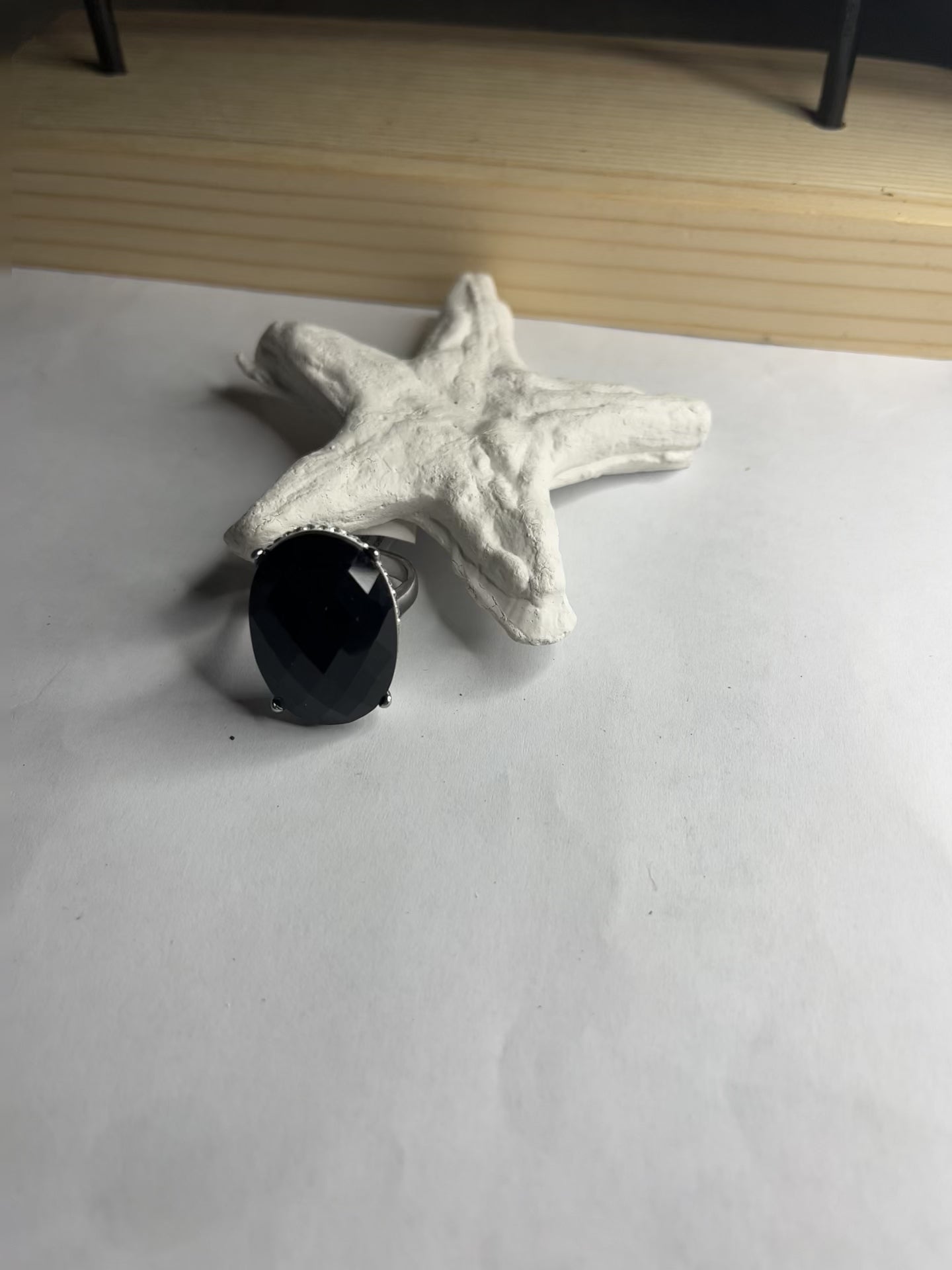 Anello con pietra nera ovale lucida e montatura argentata o dorata decorata, appoggiato su stella marina bianca