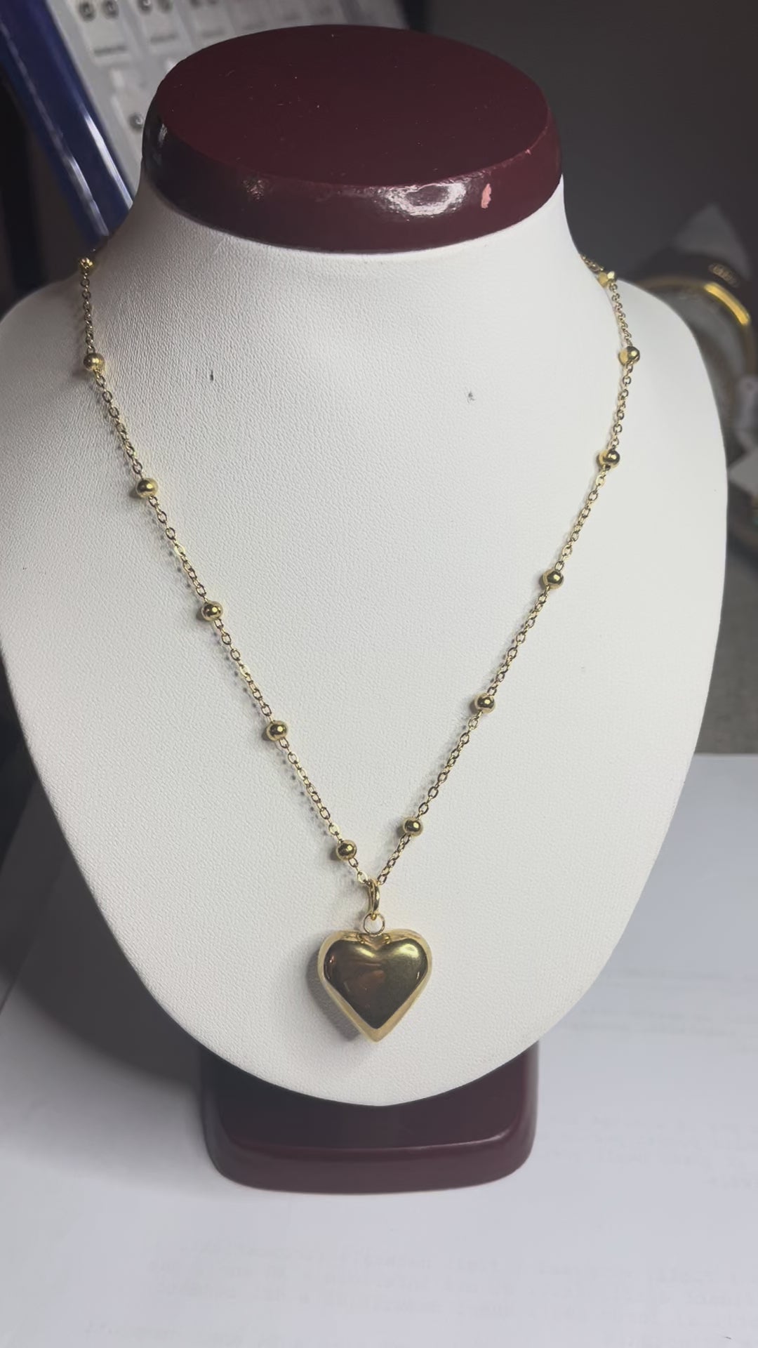 Collana Allegra in acciaio premium con catena decorata da sfere e ciondolo cuore, variante placcato oro, esposta su busto espositore bianco