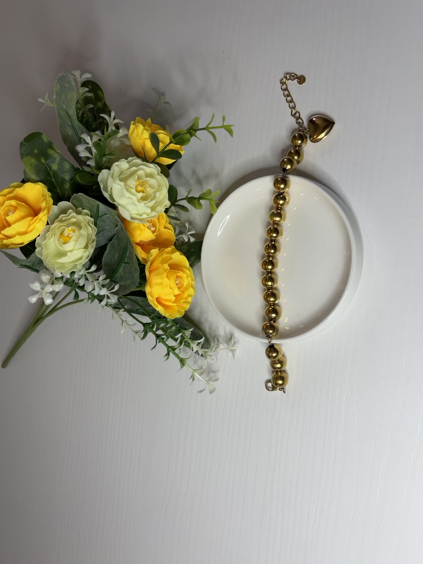 Elegante braccialetto con sfere dorate lucide su fiori gialli e foglie verdi