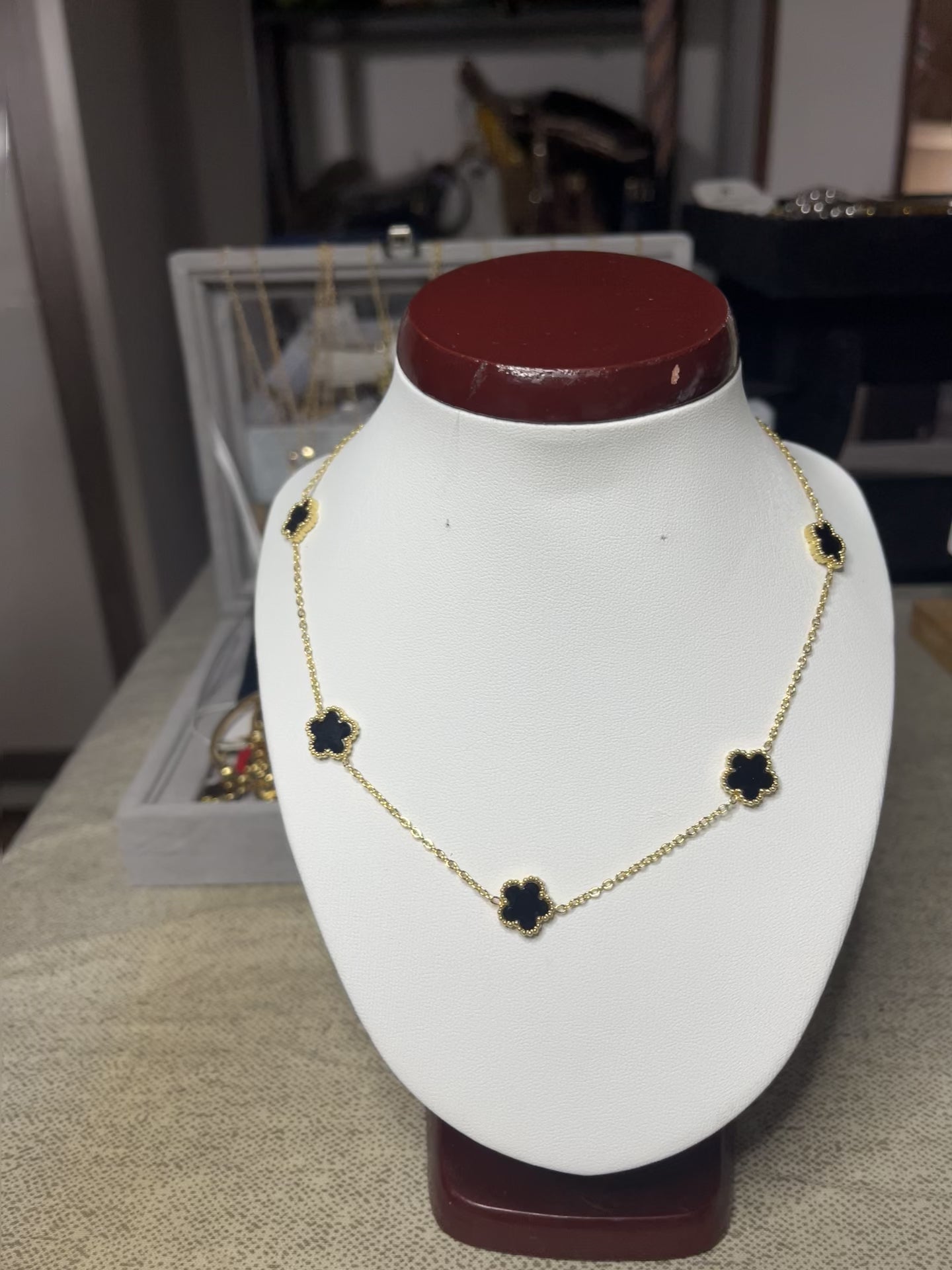 Collana Élégance Suprême in ottone dorato con cinque elementi floreali neri disposti simmetricamente, esposta su busto bianco, design elegante e raffinato stile italiano