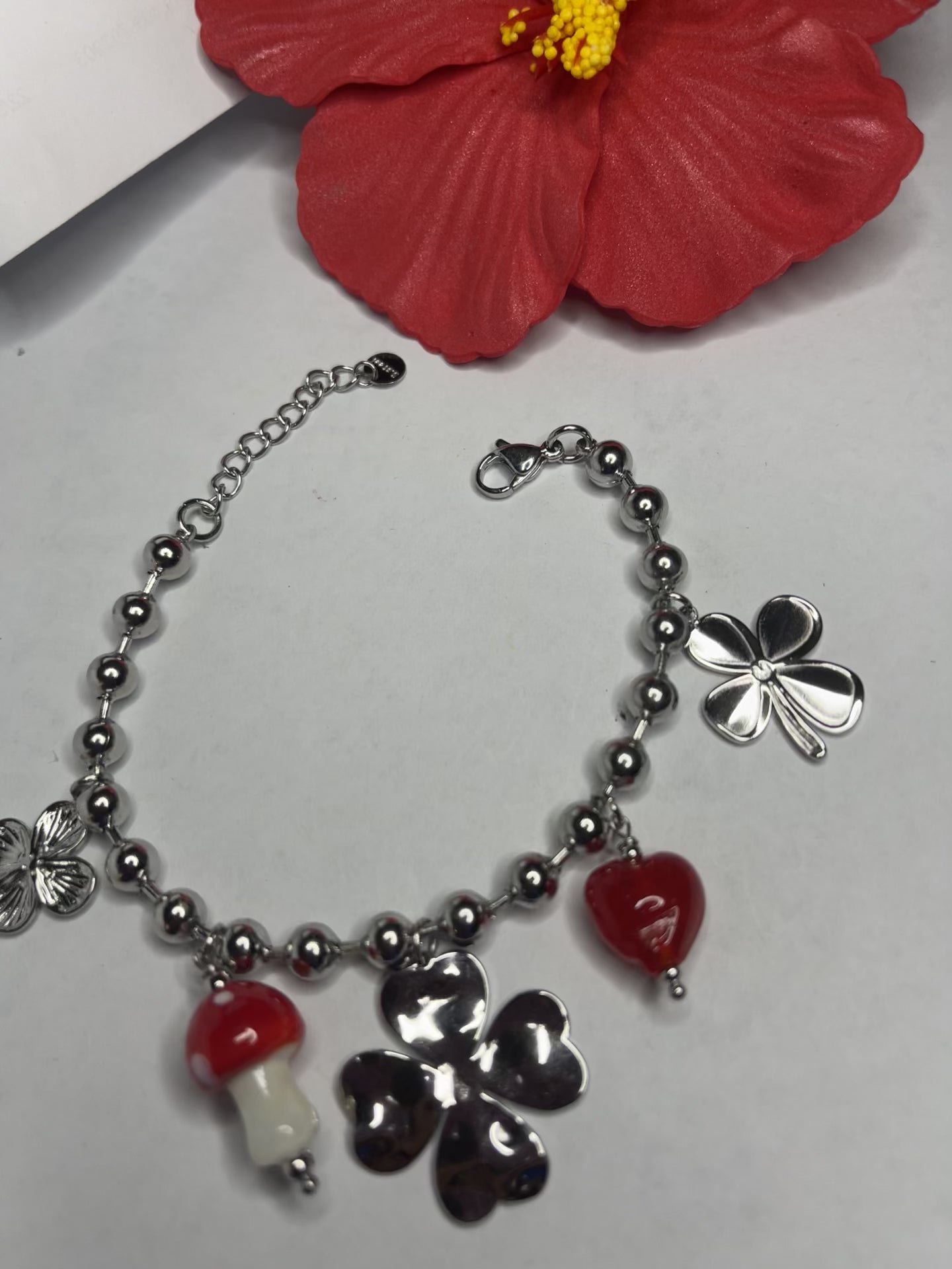 Braccialetto Giardino Magico in acciaio inox argentato con charms floreali, cuori rossi e perline colorate su sfondo grigio