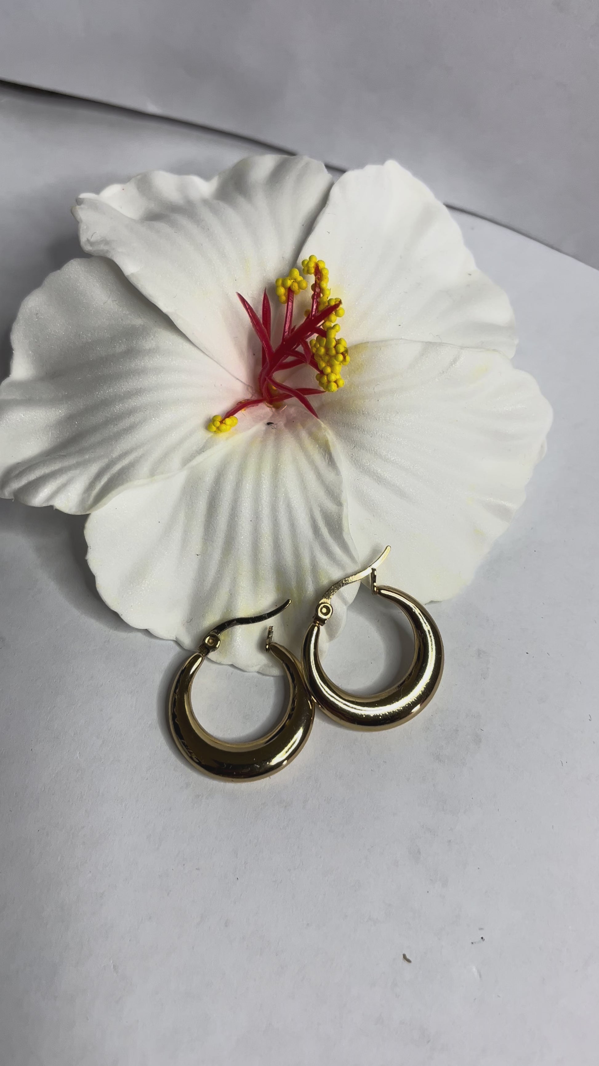 Set di orecchini creoli placcati, due paia in oro e argento, disposti su sfondo neutro con fiore rosso decorativo