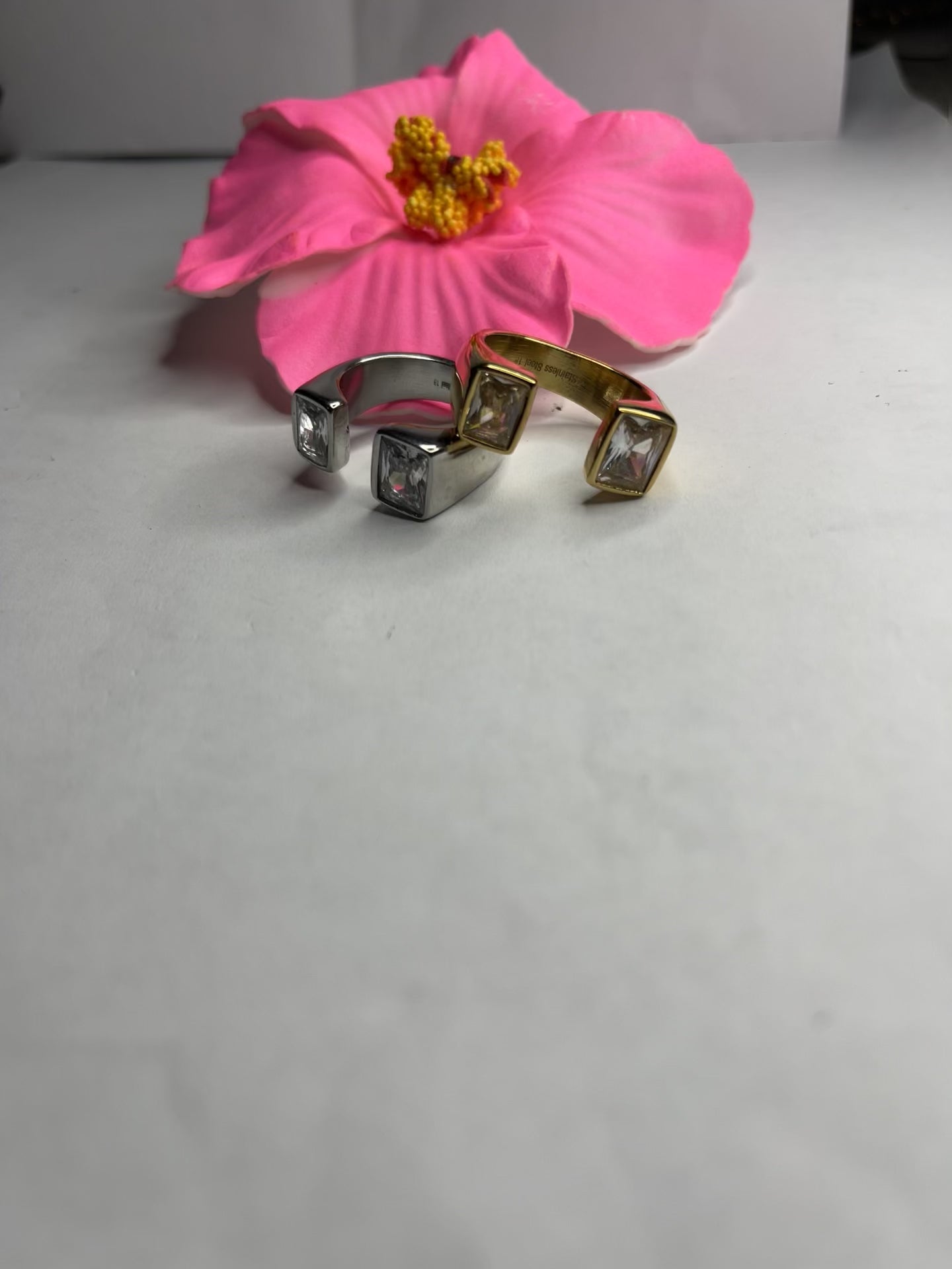 Anello Geometric Luxury con design geometrico quadrato, disponibile in versione placcata oro e argento, esposto su fiore rosa decorativo