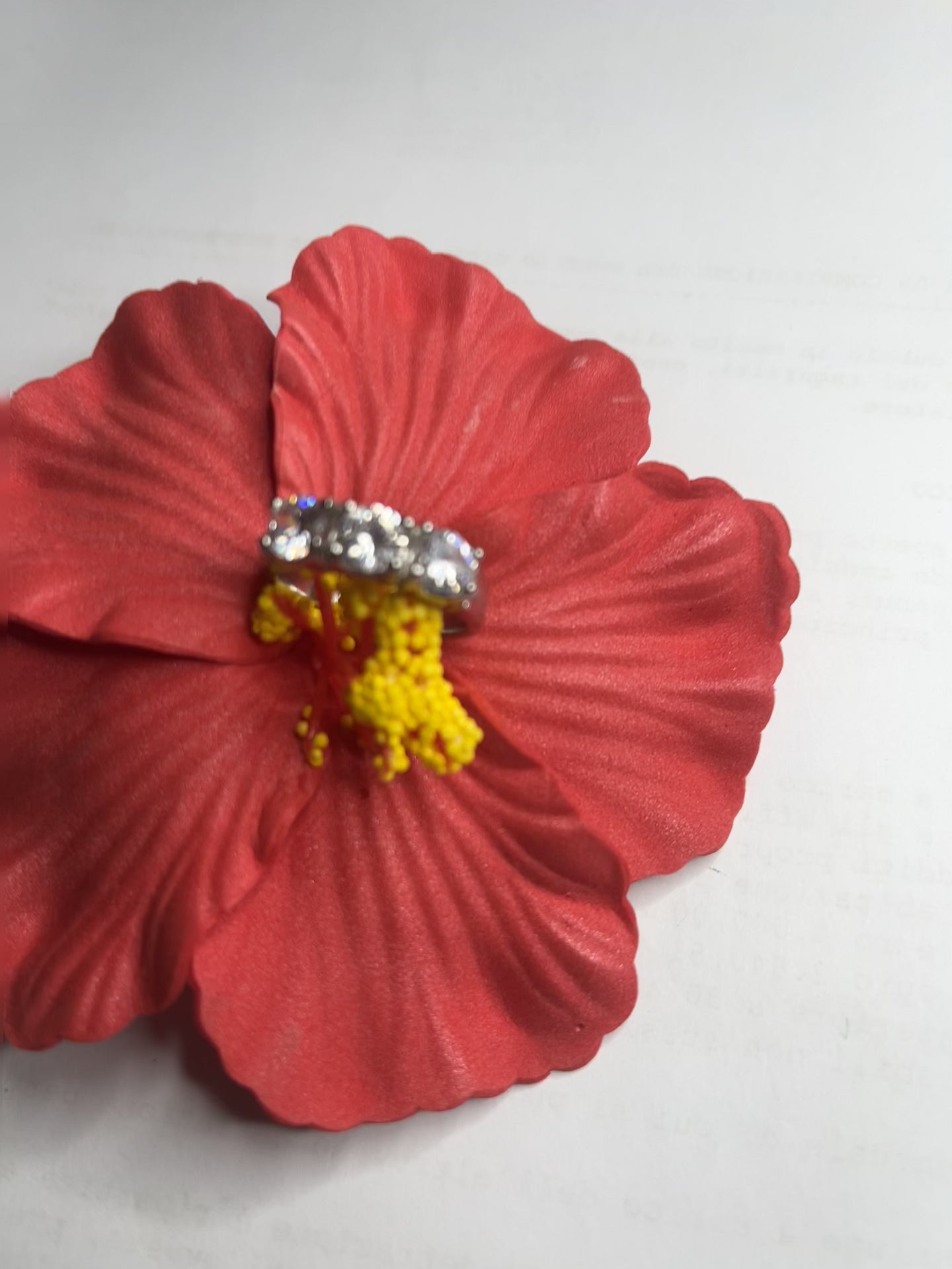 Anello Trio in acciaio premium placcato argento con tre zirconi brillanti perfettamente incastonati, fotografato su fiore rosso