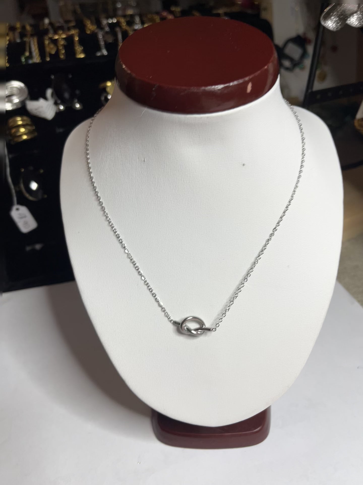 Collana Love Knot con pendente a nodo intrecciato dorato su catena delicata, simbolo di amore eterno esposto su busto bianco