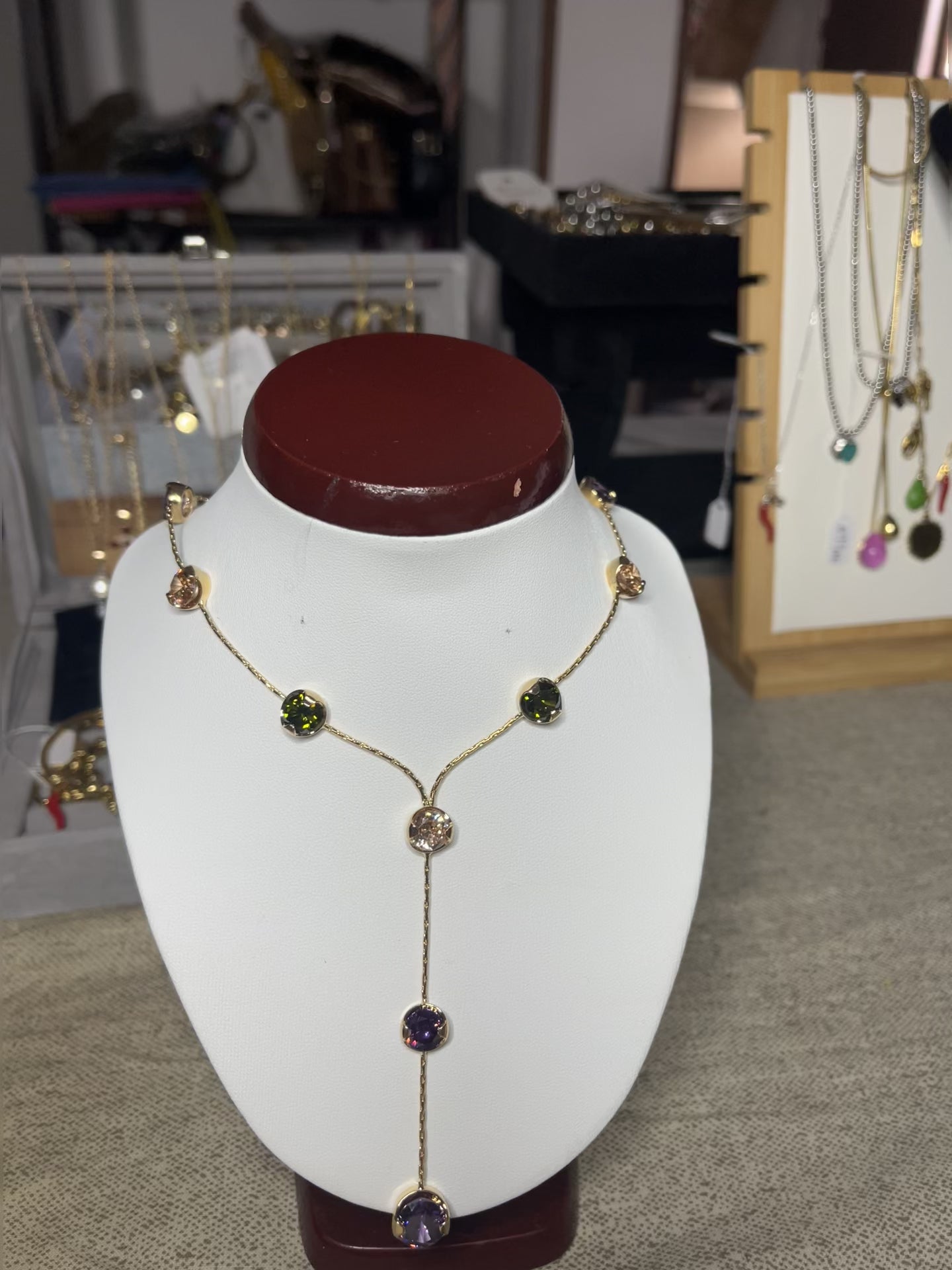 Collana Ottone e Cristalli Bohémien esposta su busto bianco, design asimmetrico con pendente lungo, cristalli verdi e viola incastonati in ottone dorato, stile bohémien elegante