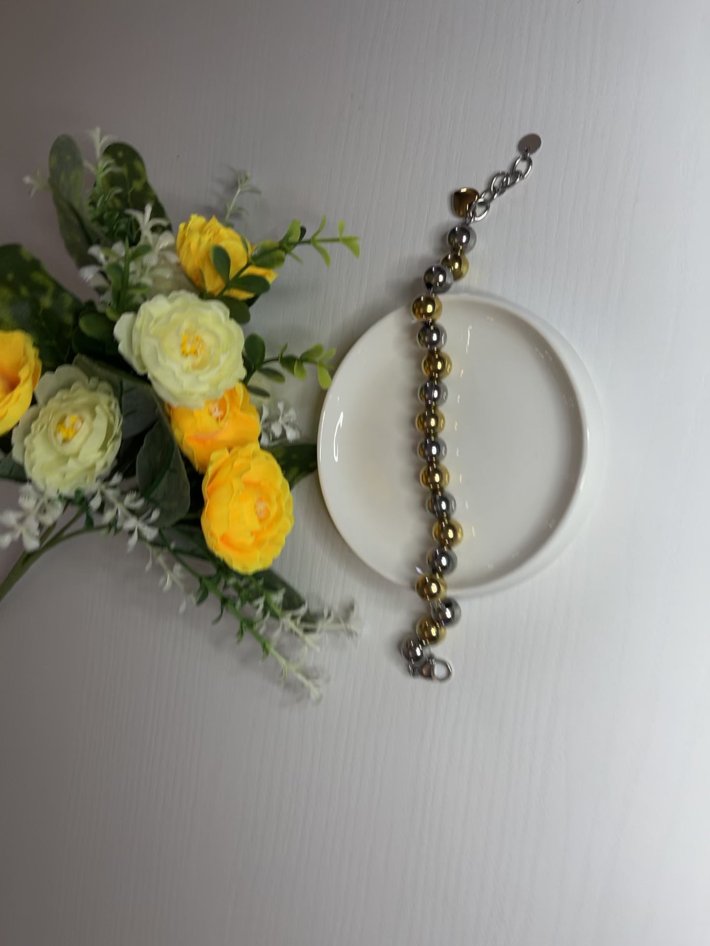 Elegante braccialetto con sfere dorate e argentate lucide su fiori gialli e foglie verdi