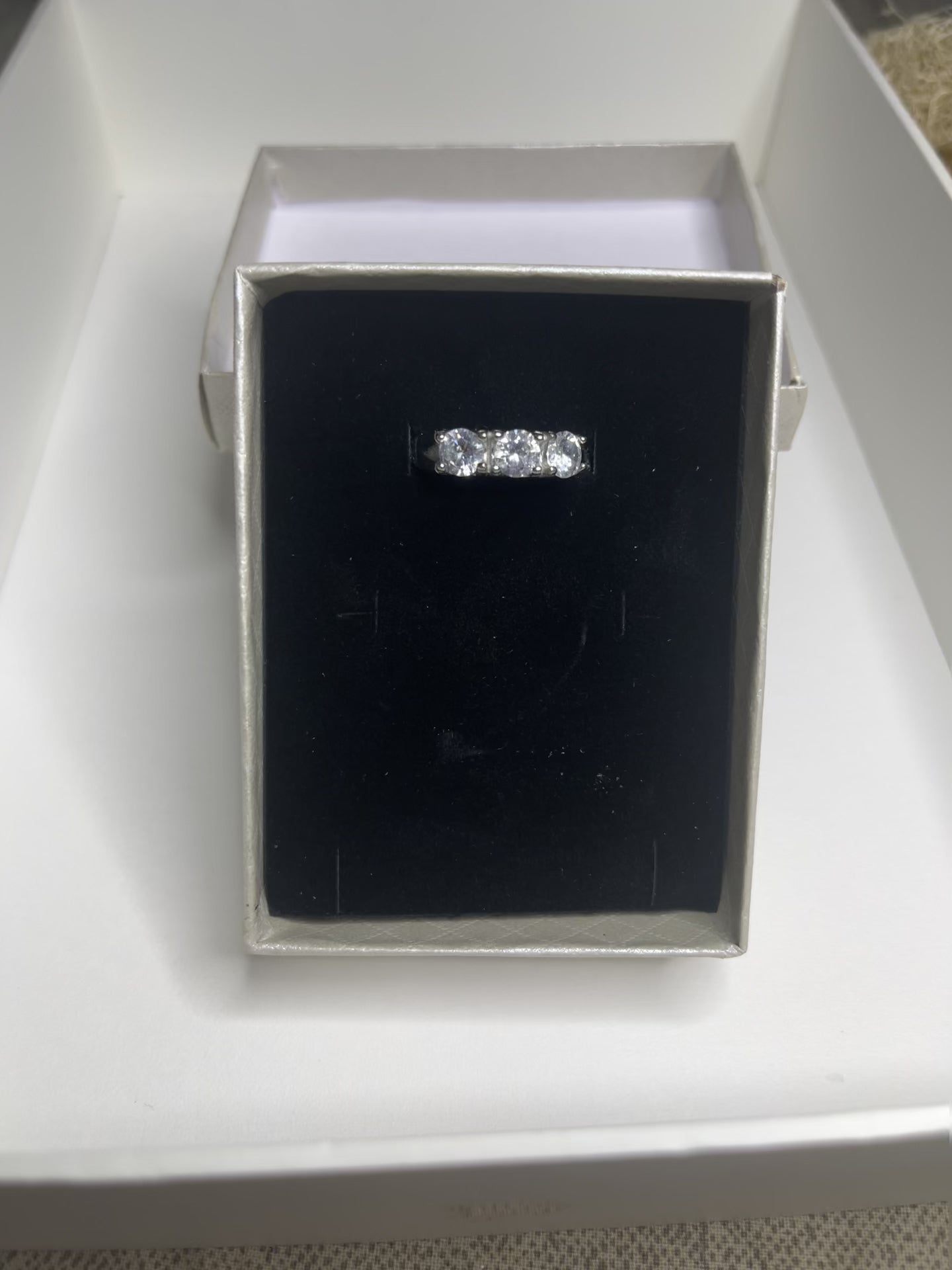 Anello Trio in acciaio premium placcato argento con tre zirconi brillanti perfettamente incastonati, fotografato su superficie scura che esalta la brillantezza delle pietre