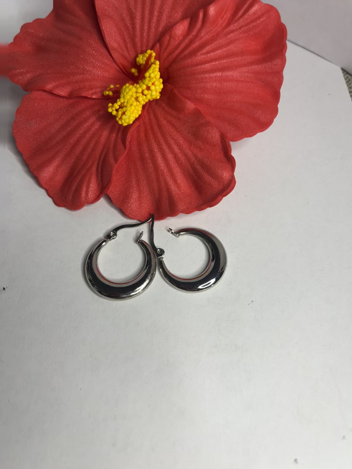 Set di orecchini creoli placcati, due paia in oro e argento, disposti su sfondo neutro con fiore rosso decorativo